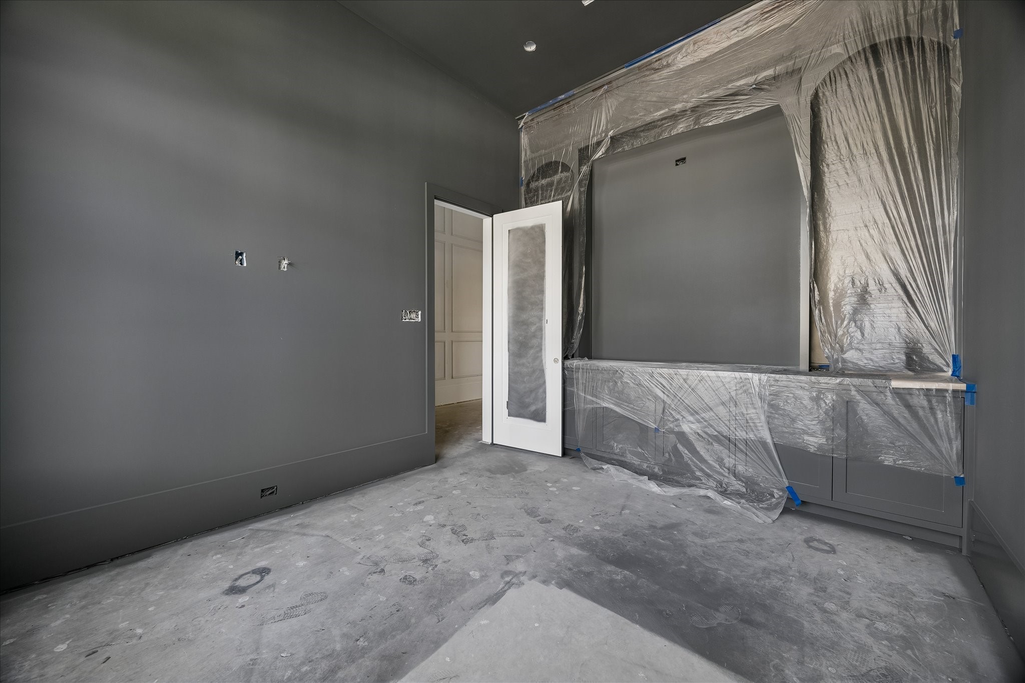 Recessed cabinetry gives the study an integrated work surface and enclosed storage, with the dark paint continuing around the room. The built in arrangement keeps work functions within the study, while protective coverings remain over the cabinetry during finish installation.