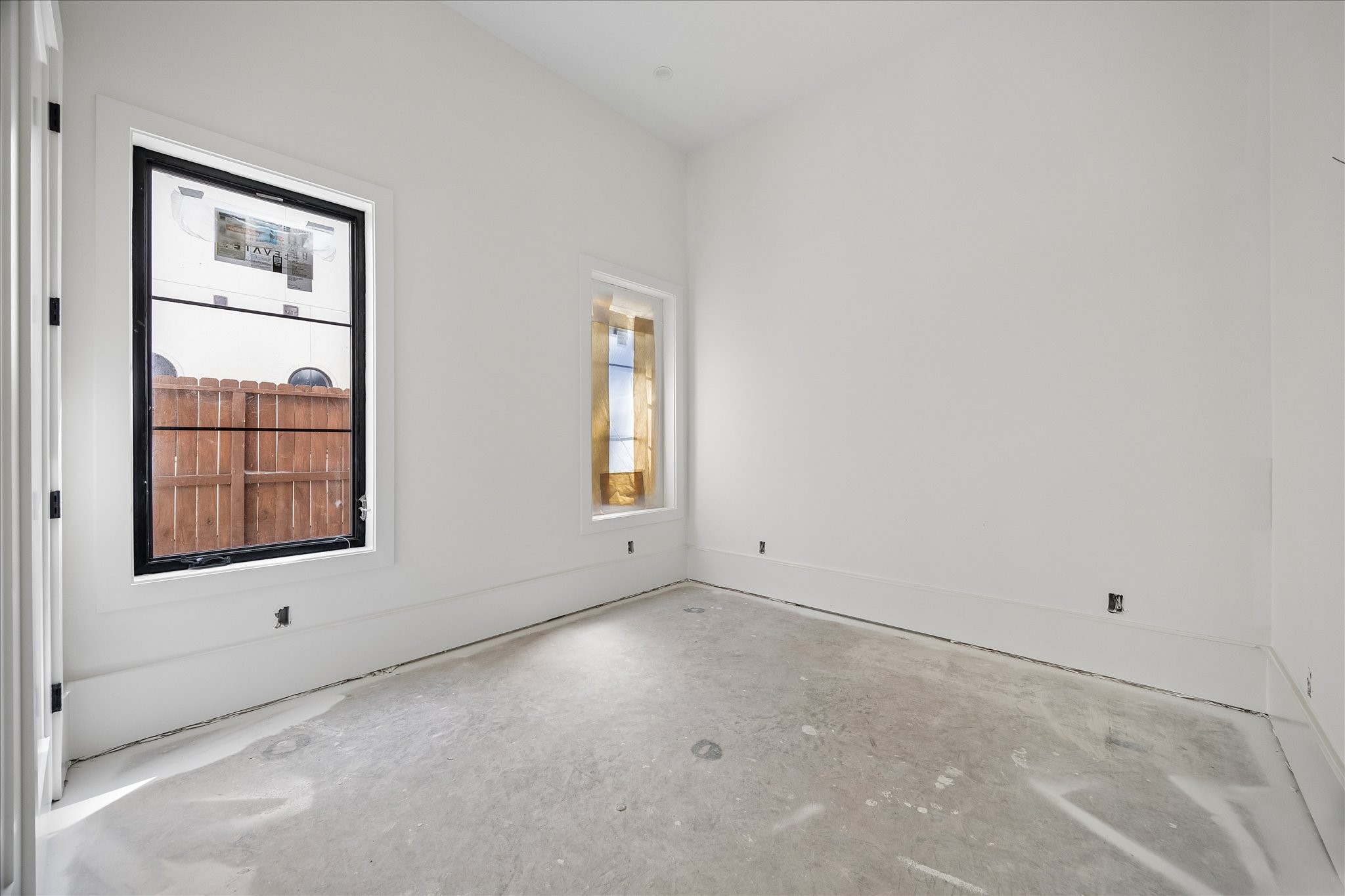 2 windows on adjoining walls bring daylight into this additional room, with broad wall space between the openings and direct hallway access. The light wall and trim palette keeps the room consistent with the adjoining spaces. Flooring and final fixtures remain in progress.