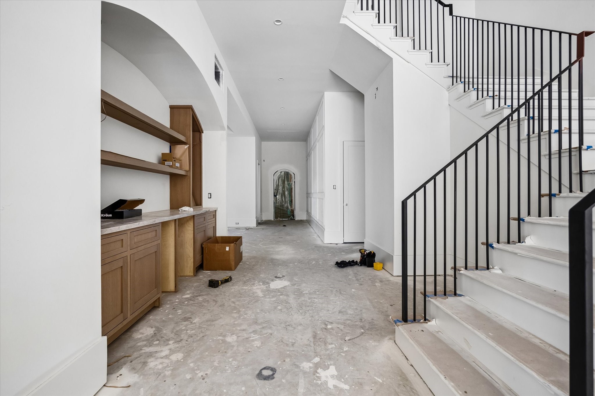 Drawers, lower cabinets and open shelves organize supplies beside the staircase, while the open hall connects the arched front entry with the main living area.