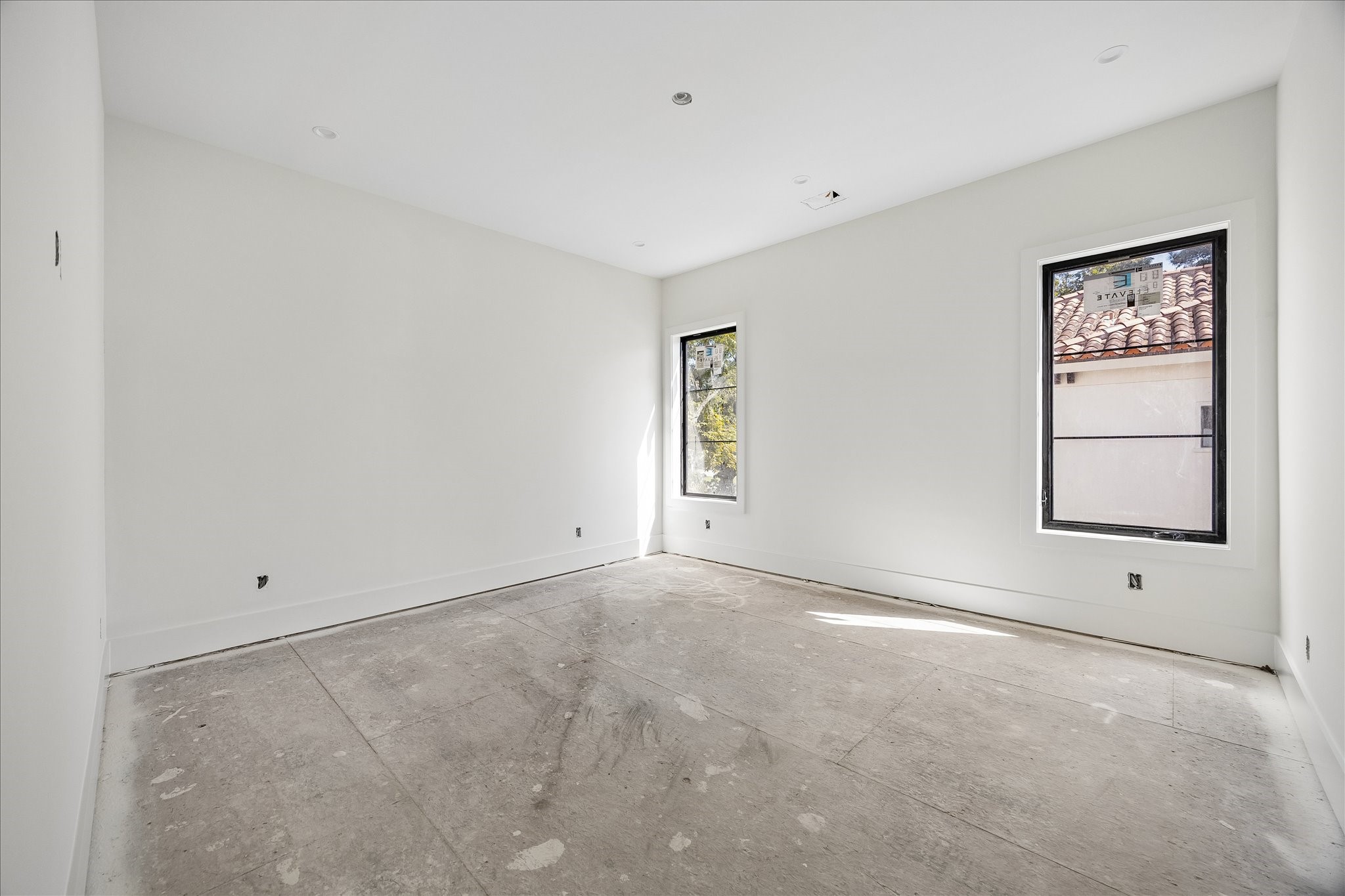 2 tall windows brighten this room while preserving a broad wall area between the openings. Deep baseboards and simple door trim continue the home's restrained interior detailing. The photograph shows the room before final flooring and fixture installation.