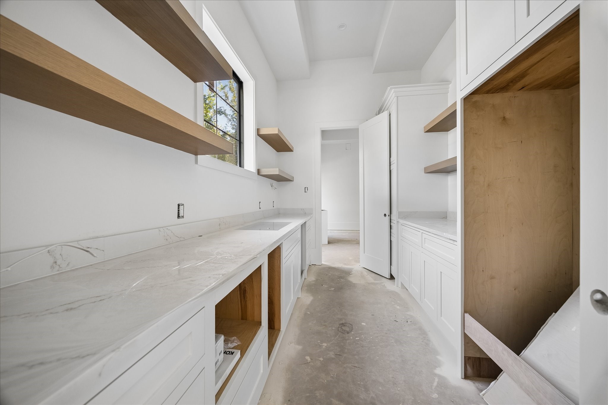 Butler's pantry provides a separate counter and storage zone between the dining room and kitchen. Long work surfaces, open wood shelves, lower drawers and tall cabinetry add capacity for preparation and serving while keeping supplies outside the main living area.