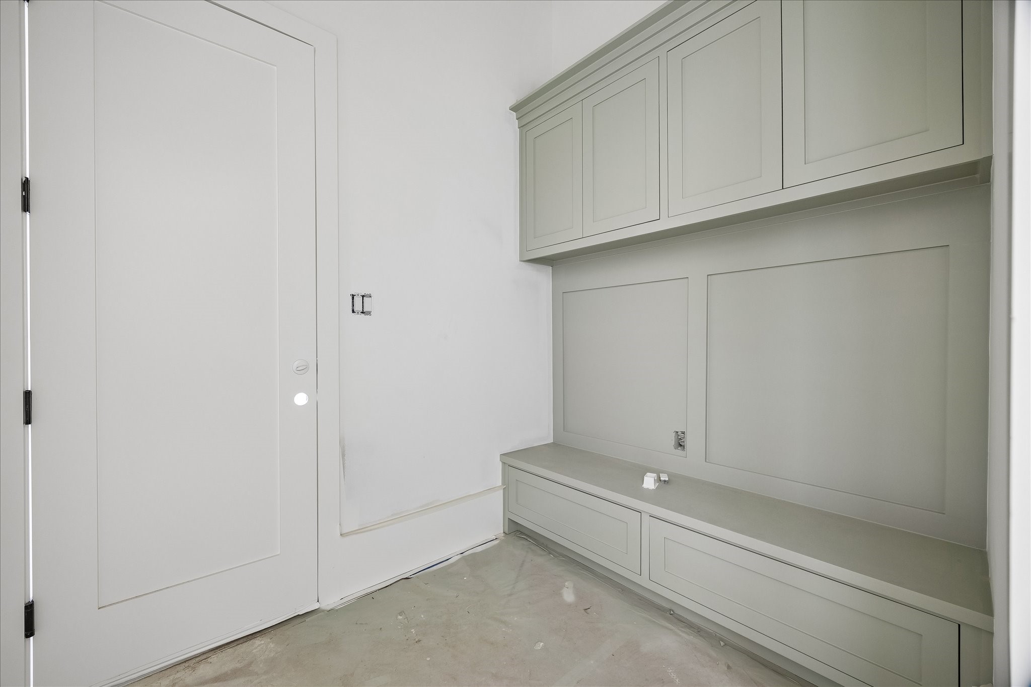 Built in bench storage creates a practical drop zone beside the door, with drawers below and cabinets overhead. Paneled detailing ties the storage wall together, providing a place to set down daily items and organize supplies without extending into the circulation space.