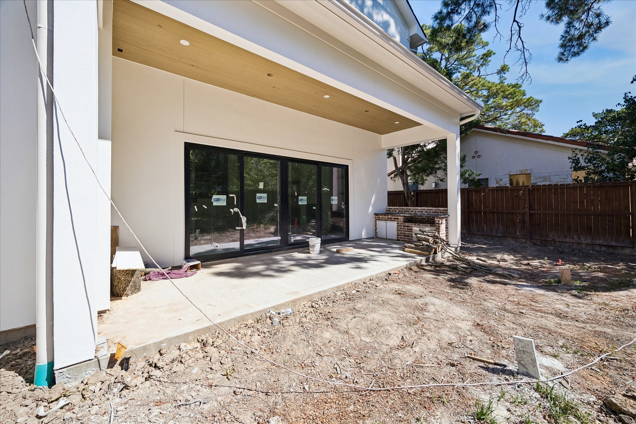 Covered rear porch pairs a stained beadboard ceiling and recessed lights with broad doors to the living room. The brick counter structure defines the planned outdoor kitchen. A 40 inch natural gas grill and sink are specified; installation and yard work remain in progress.