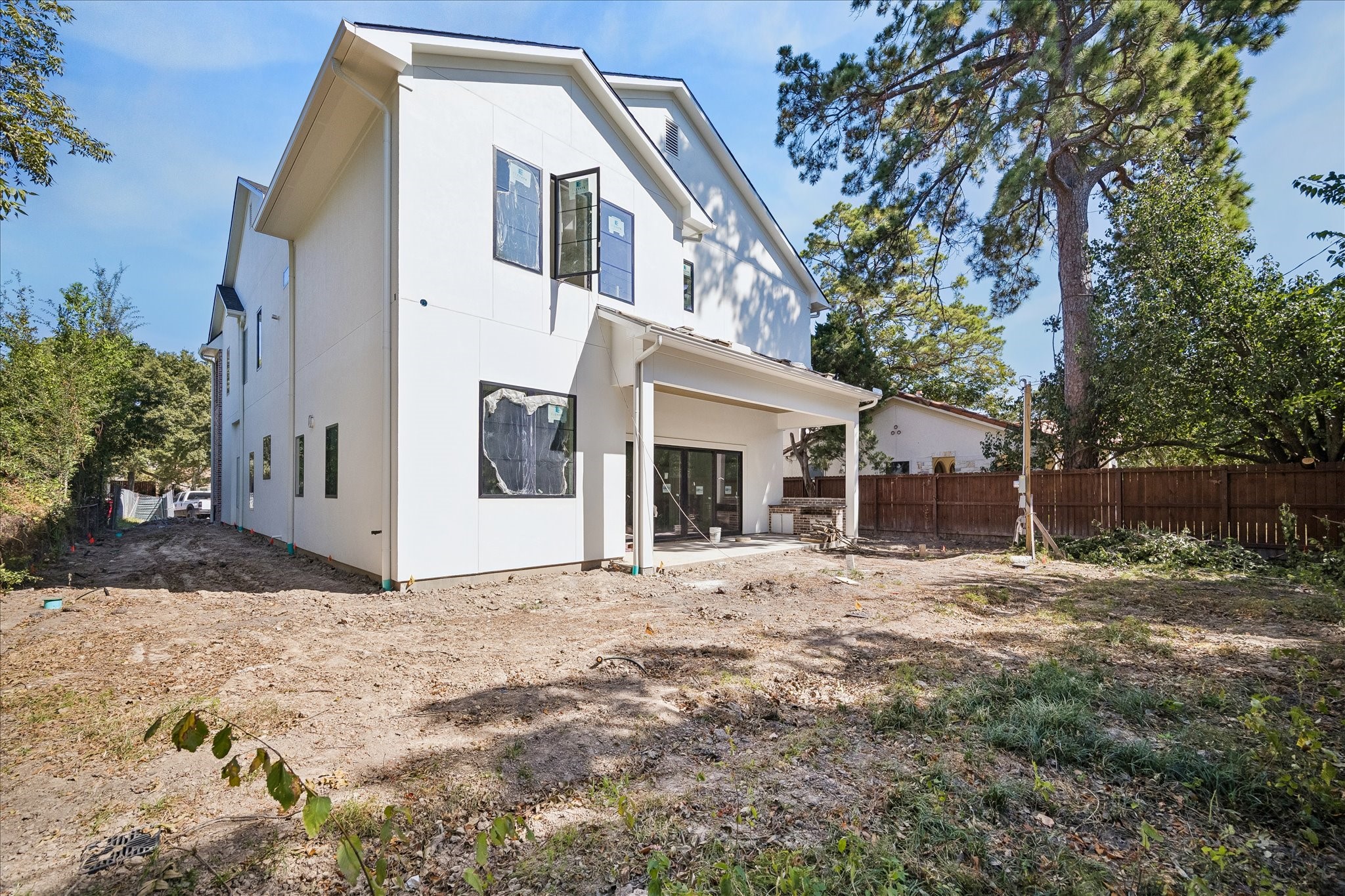 Rear elevation views place the covered porch beside the open backyard and side yard. Broad windows and sliding doors connect the interior to the outdoor space. Plans route utilities along the side to preserve backyard flexibility; landscaping remains in progress.