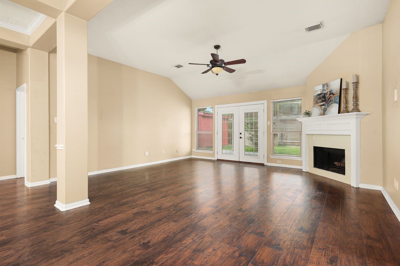 Spacious Living Area with High Ceiling, Beautiful Wood-Look Flooring, Fireplace, and French Doors Leading to the Covered Patio.