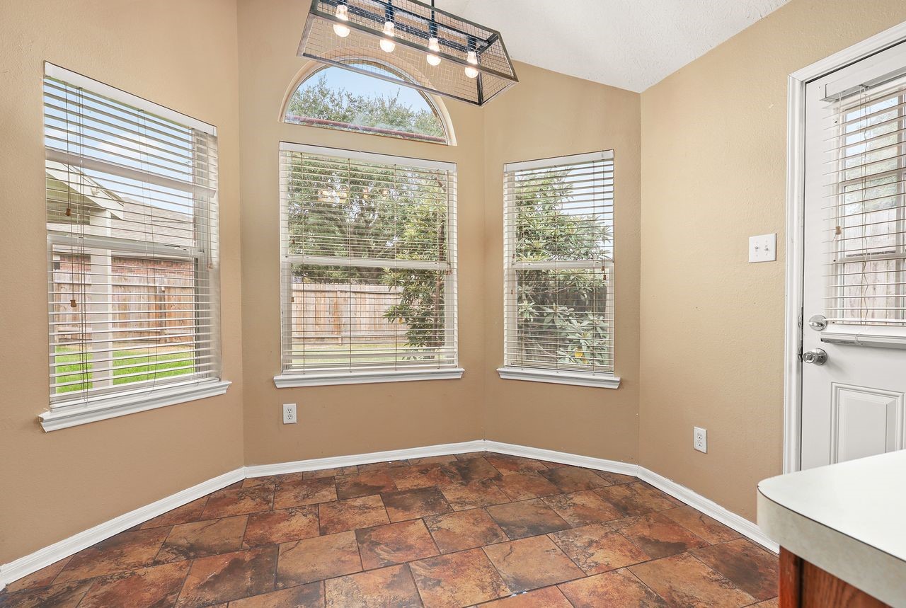 Bright and Cheerful Breakfast Nook Features High Ceiling, Beautiful Arched Window, and Multiple Windows Overlooking the Backyard.
