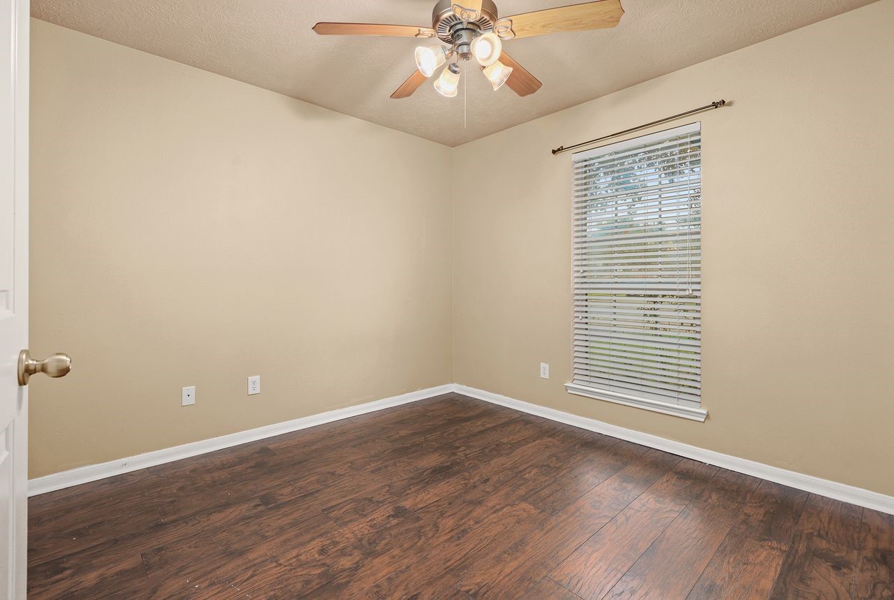 Secondary Bedroom Features Wood-Look Flooring, Ceiling Fan, and Window with Faux Wood Blinds.