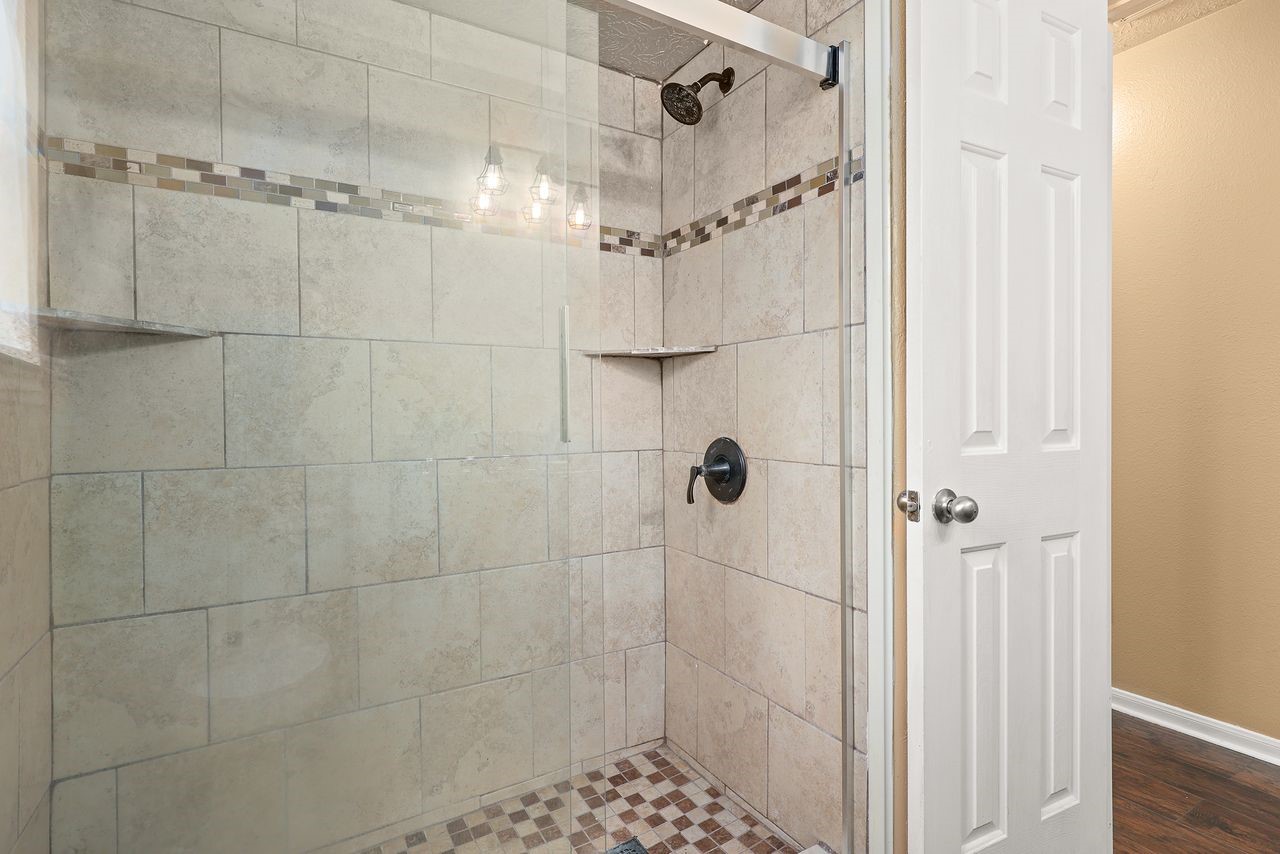 Beautifully Tiled Oversized Shower with Decorative Accents, Glass Enclosure, and Built-In Corner Shelves.