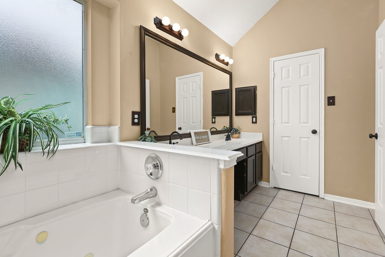 Primary Bath Features a Relaxing Jetted Tub, Dual-Sink Vanity, High Ceiling, and Natural Light.