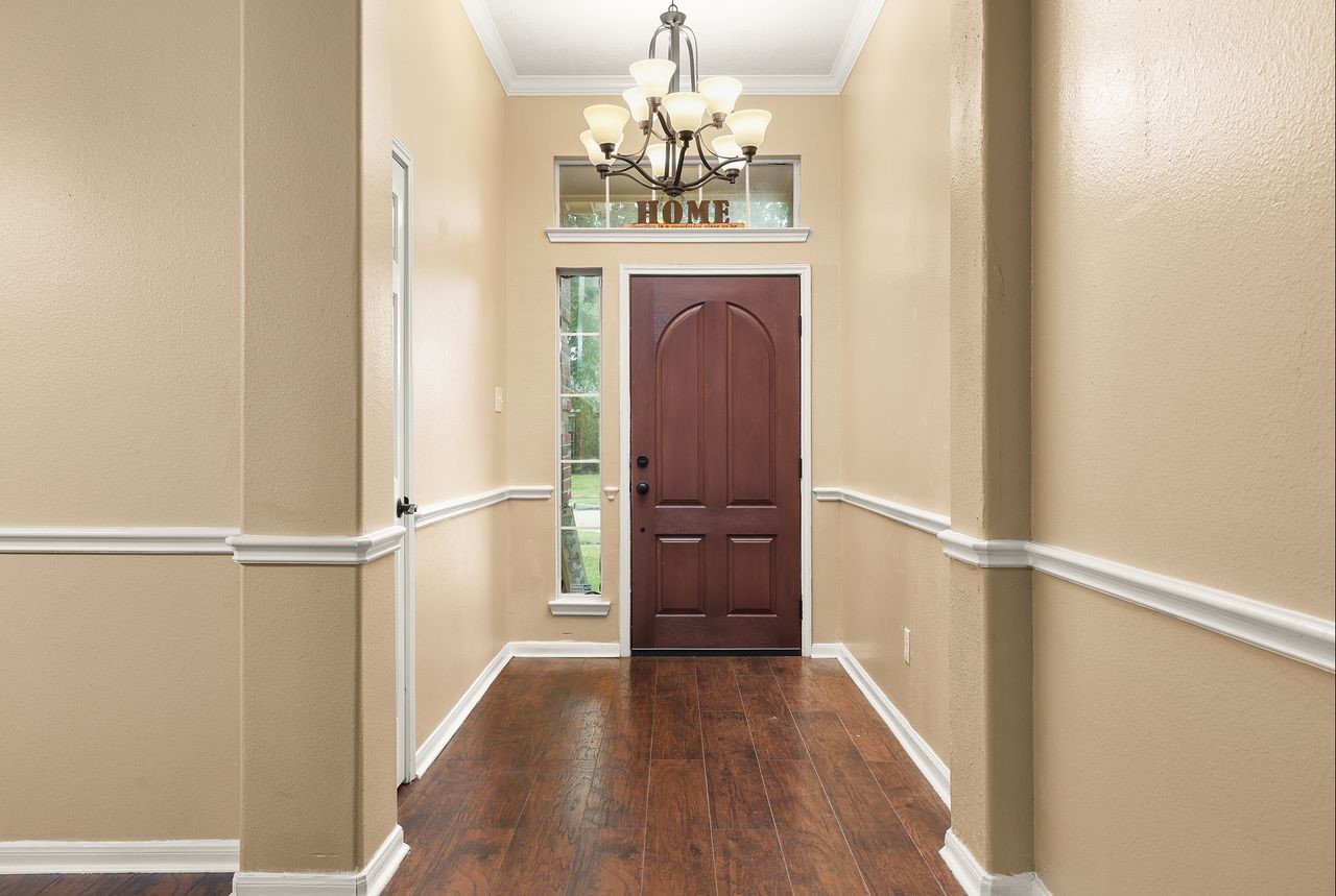 Welcoming Entry Features Beautiful Wood-Look Flooring, Elegant Chandelier, Decorative Chair Rail Molding, and High Ceiling.
