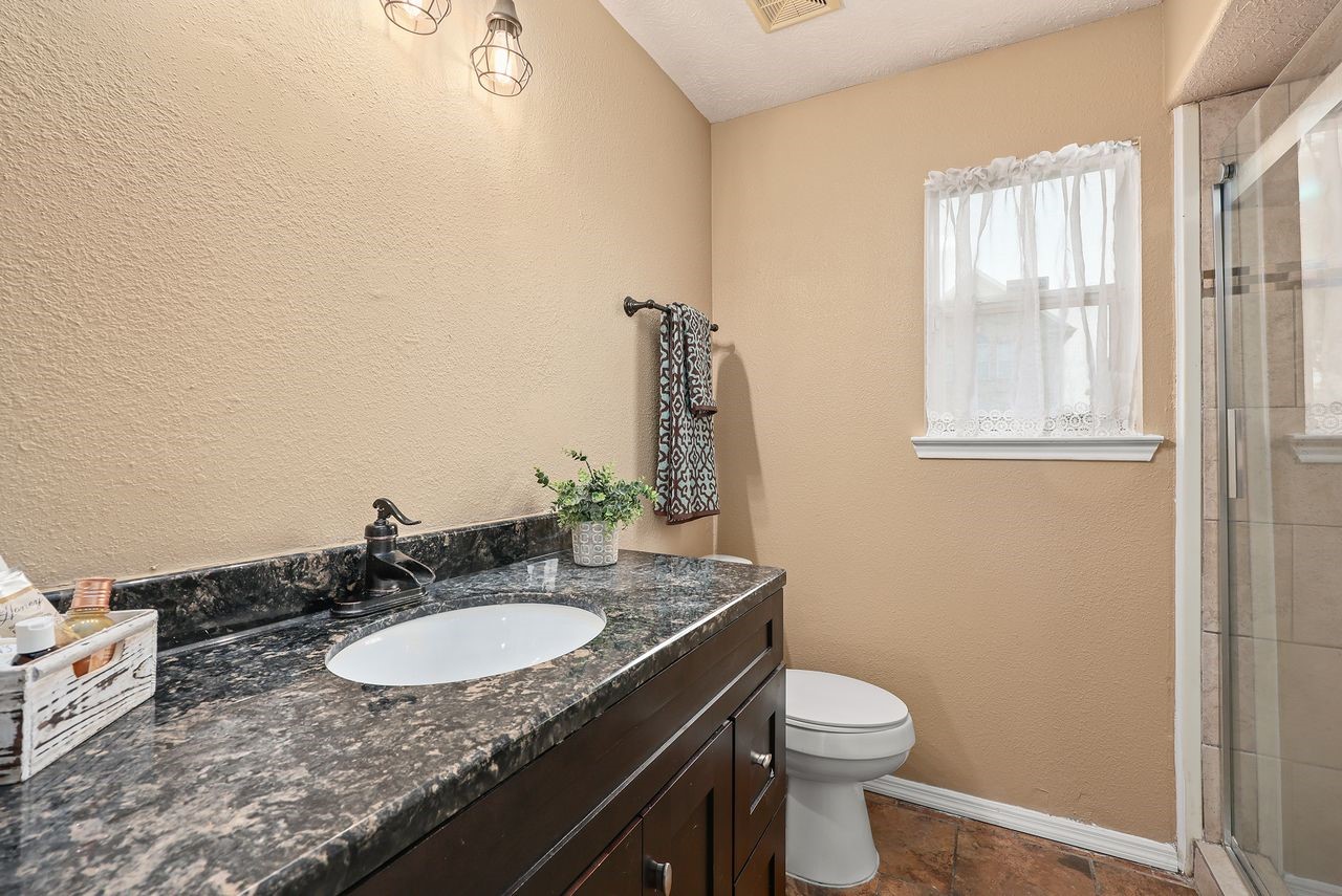 Nicely Appointed Guest Bath Features a Beautiful Granite Countertop, Dark Wood Vanity, Updated Fixtures, and an Oversized Tiled Shower with Glass Enclosure.