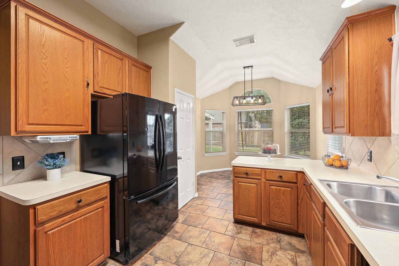 Another View of the Kitchen Showcasing the Refrigerator, Generous Storage, and Bright Breakfast Nook with High Ceiling.