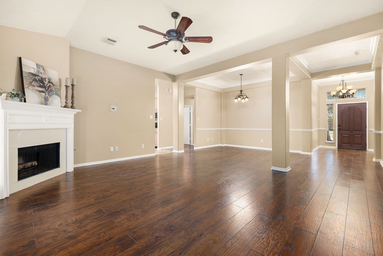 Open Living and Dining Area Features Rich Wood-Look Flooring, High Ceilings, Decorative Molding, and a Cozy Fireplace.