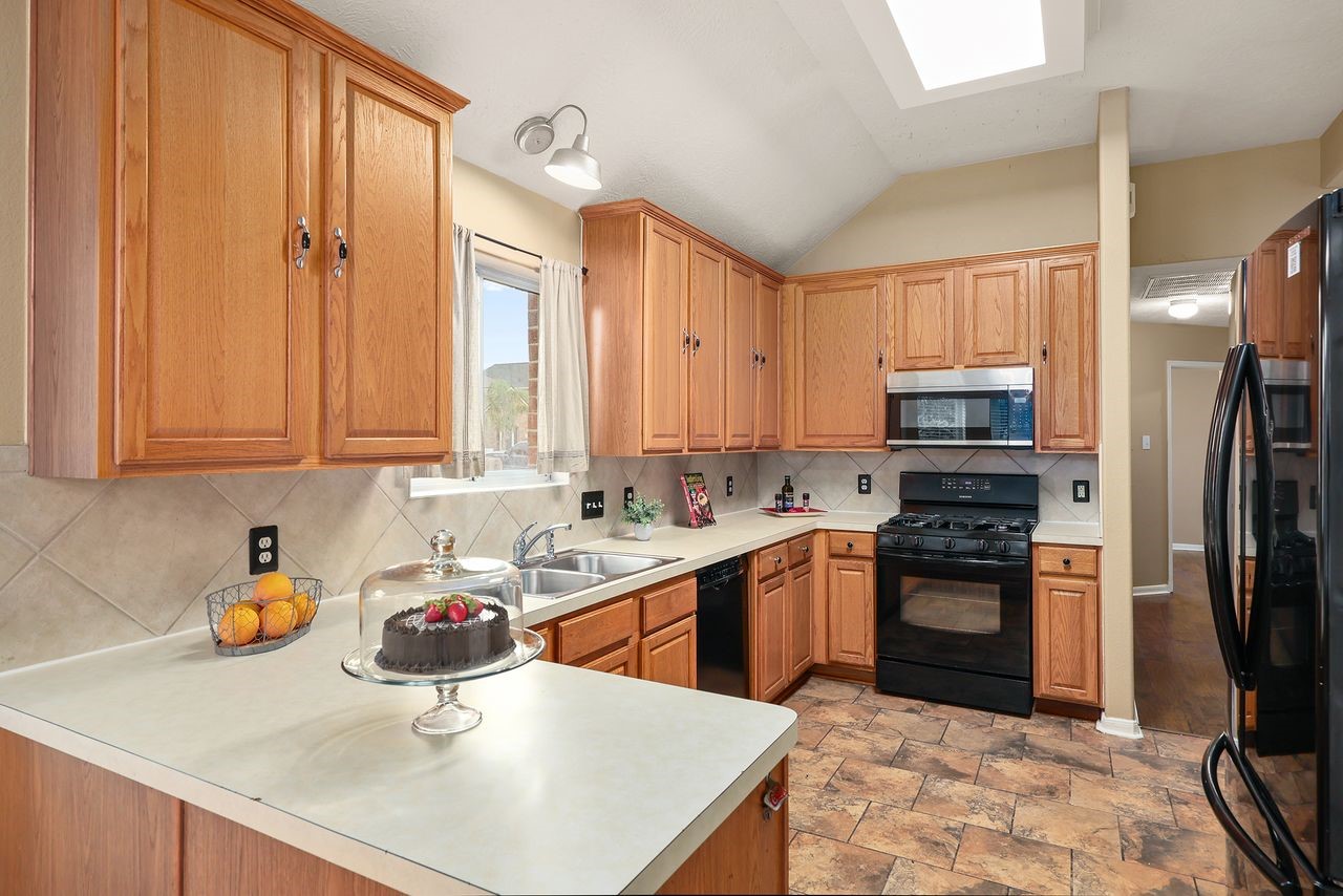 Spacious Kitchen Features Abundant Cabinet and Counter Space, Breakfast Bar, Pantry, and Black Appliances.