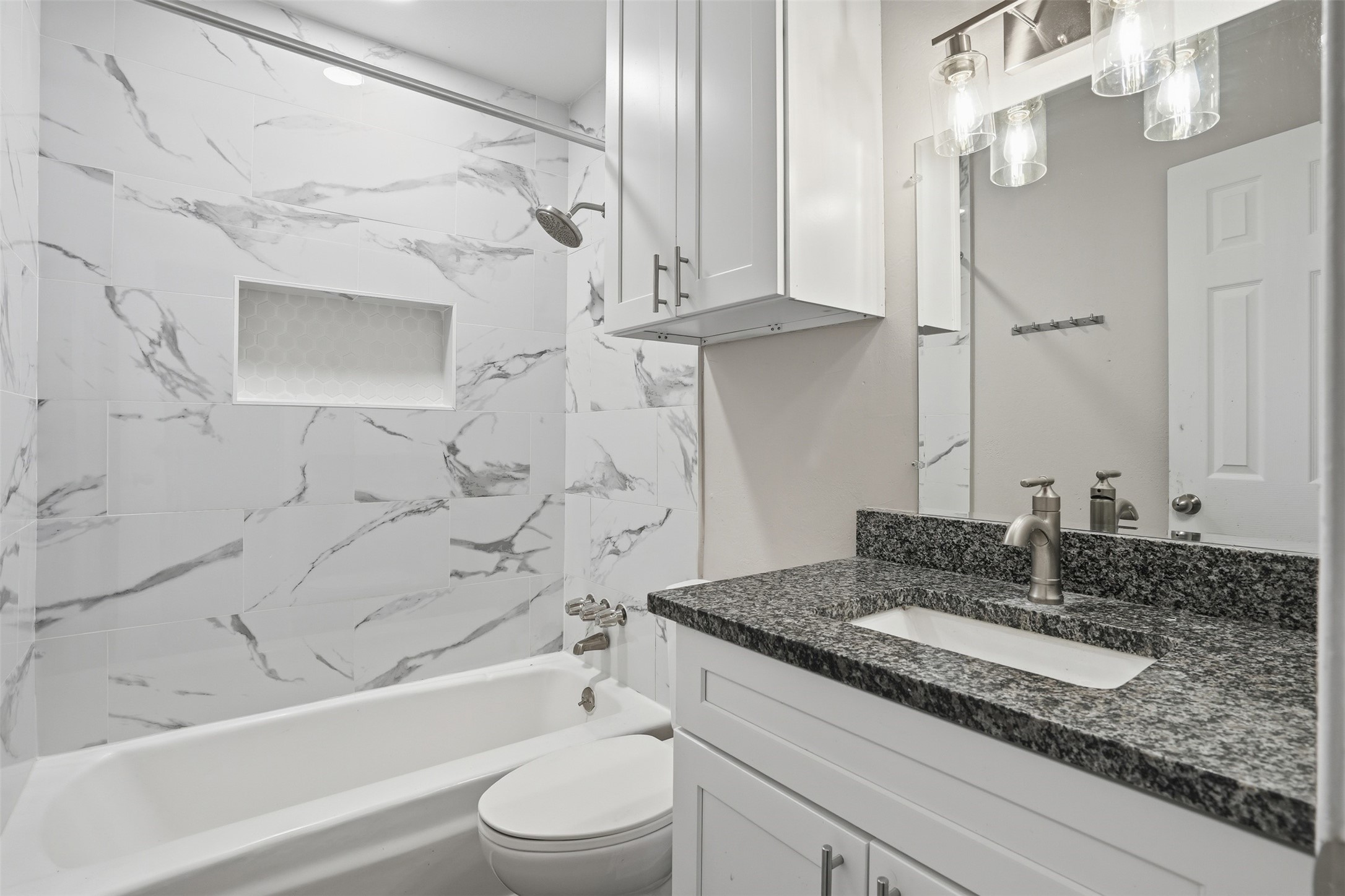Bright and modern bathroom featuring a tub/shower combination with elegant marble-style tile and a granite countertop vanity.