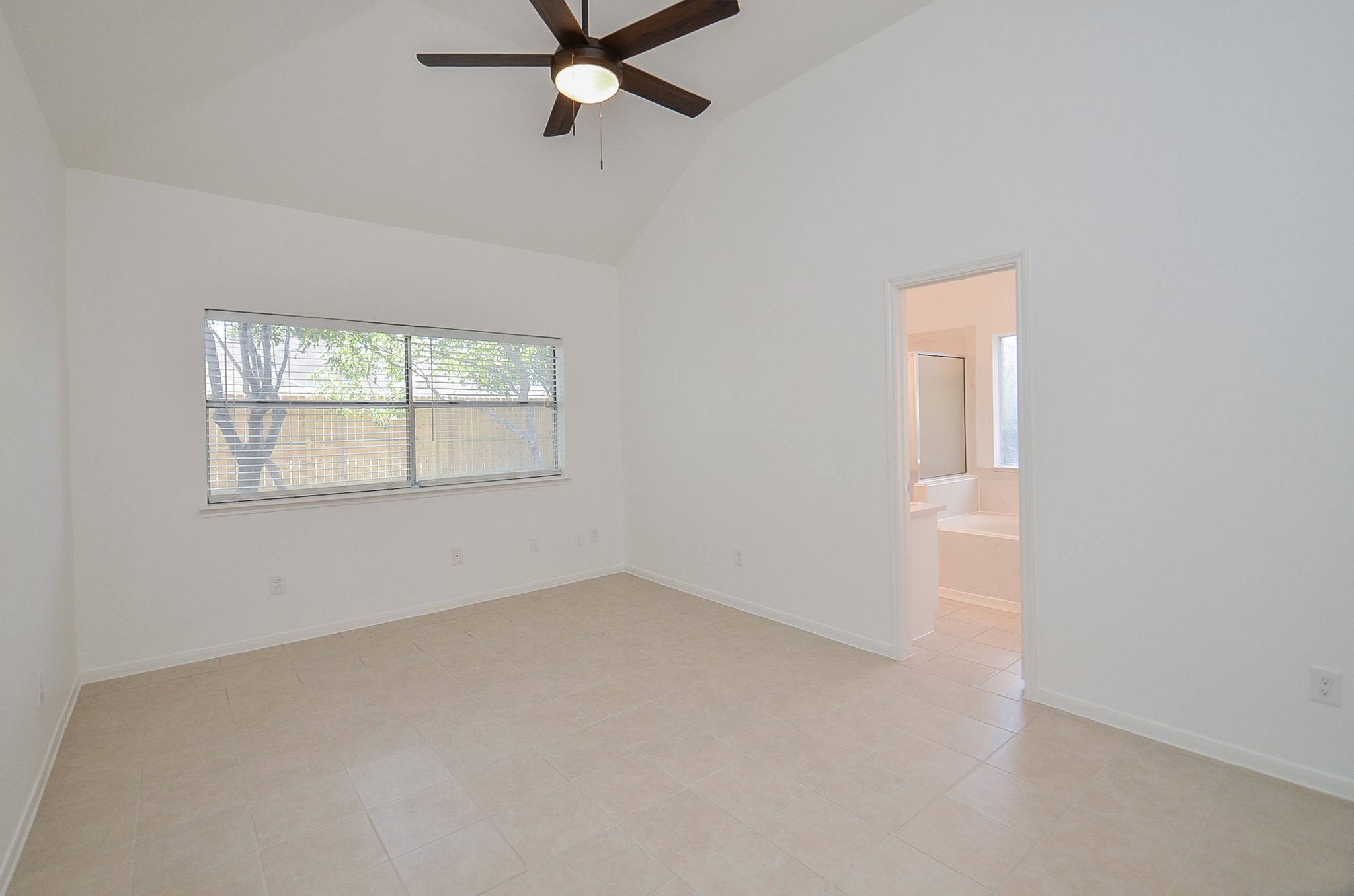 Large primary room with high ceilings, no carpet and ceiling fan.