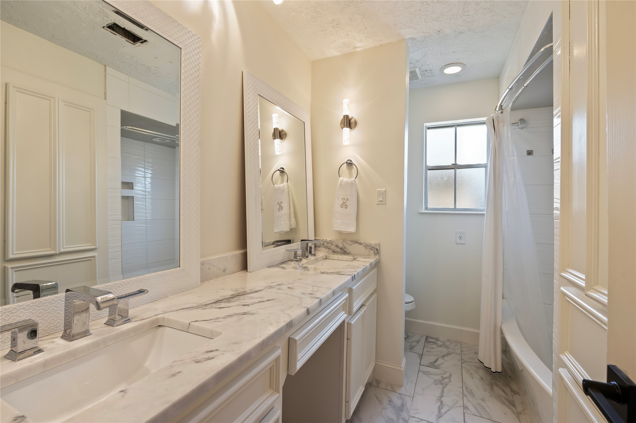Full sized secondary bath with his/her vanities, large vanity mirror, tile flooring and more.