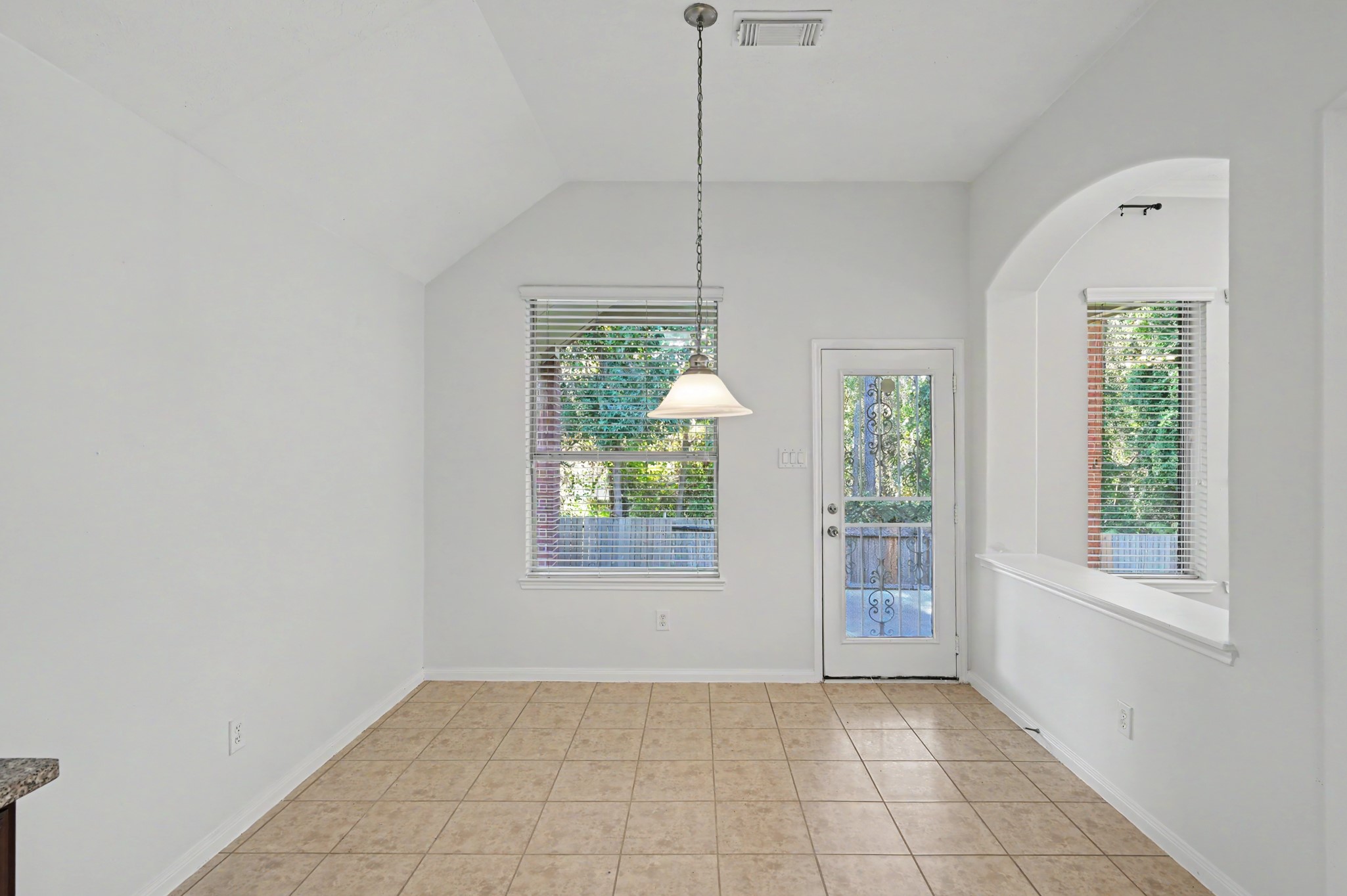 Bright breakfast area featuring vaulted ceilings, tile flooring, pendant lighting and backyard views with convenient outdoor access.