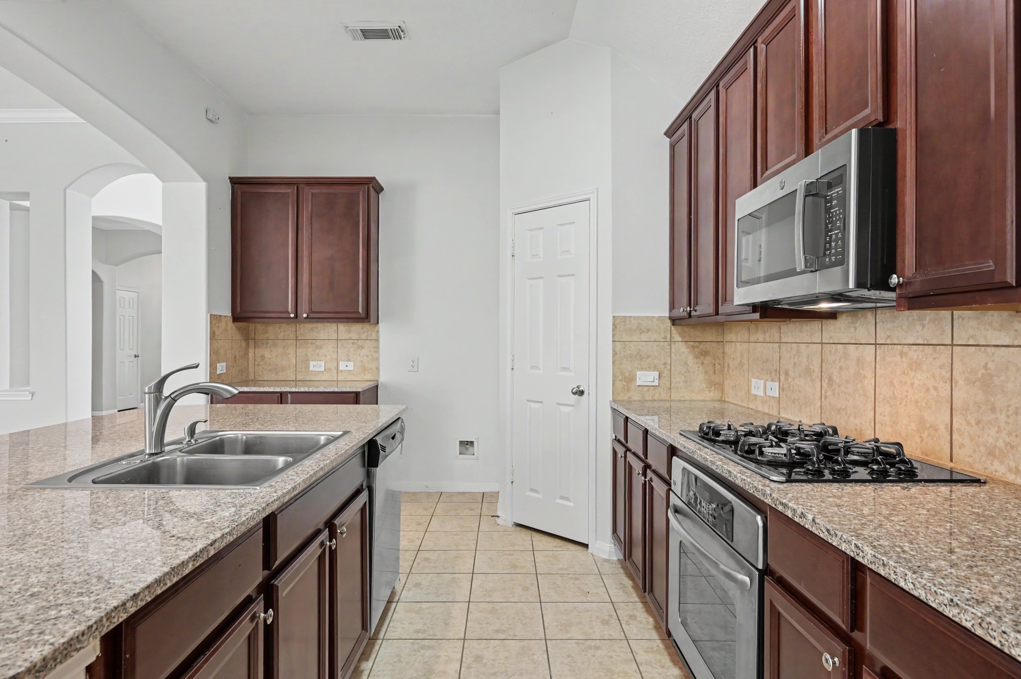 Island kitchen featuring granite countertops, double sink, stainless steel appliances, gas cooktop, tile backsplash and ample cabinetry for storage.