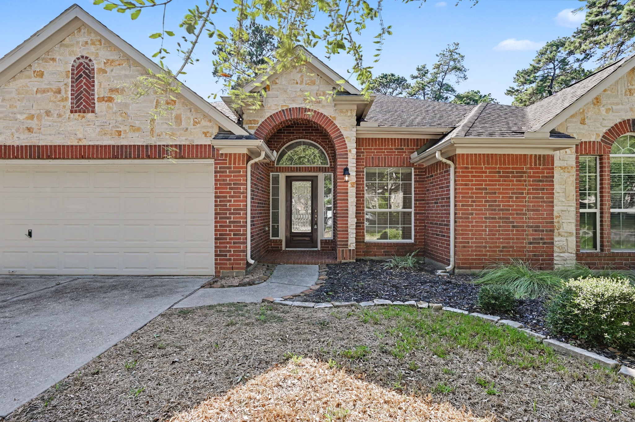 Inviting covered front entry featuring an elegant brick archway, decorative glass front door with sidelights, arched transom window and attractive stone accents, creating a warm and welcoming first impression.