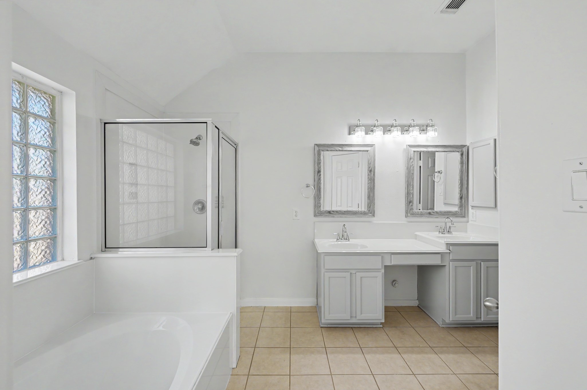 Spacious primary bath featuring dual vanities, soaking tub, separate glass-enclosed shower and decorative glass block window.