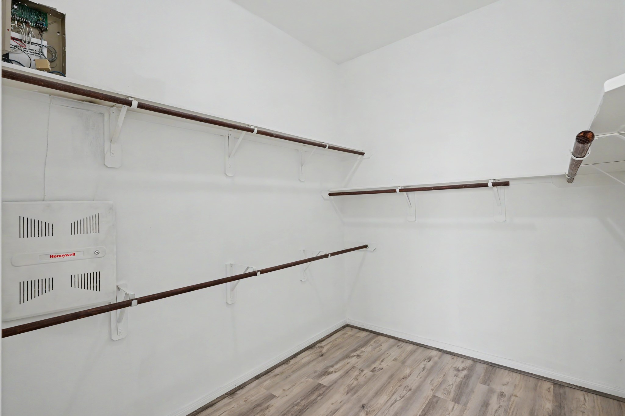 Spacious primary walk-in closet featuring multiple hanging rods, built-in shelving and wood-look flooring for convenient organization.