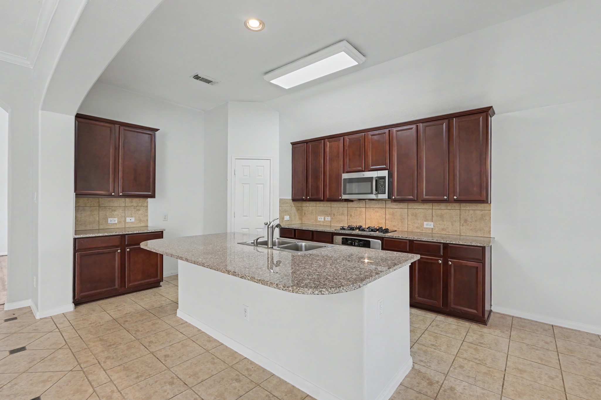 Spacious island kitchen featuring granite countertops, 42" cabinetry, stainless steel appliances, gas cooktop, tile backsplash and corner pantry.