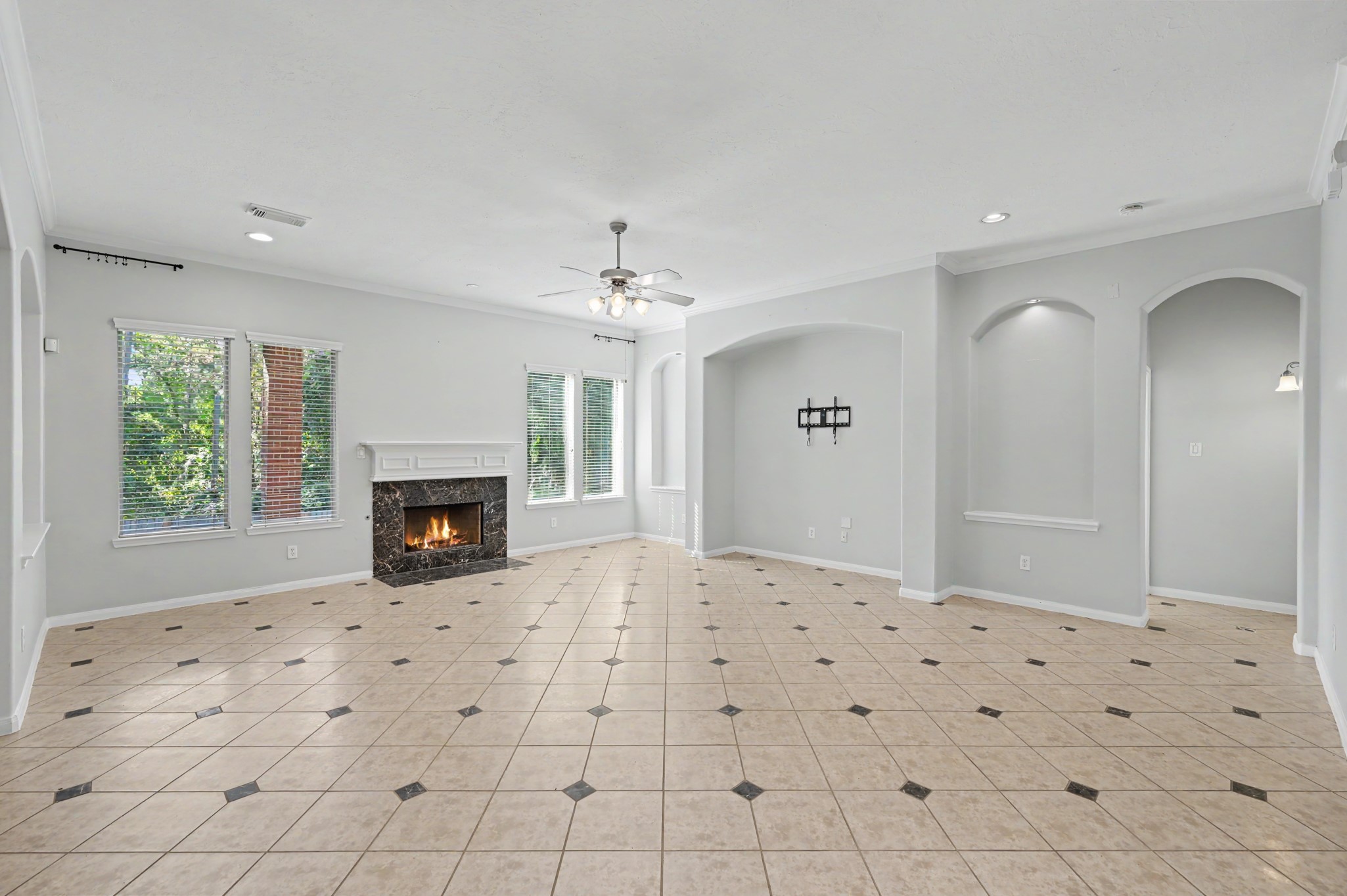 Spacious family room featuring decorative tile flooring, crown molding, cozy fireplace, abundant natural light and an open-concept layout perfect for entertaining.