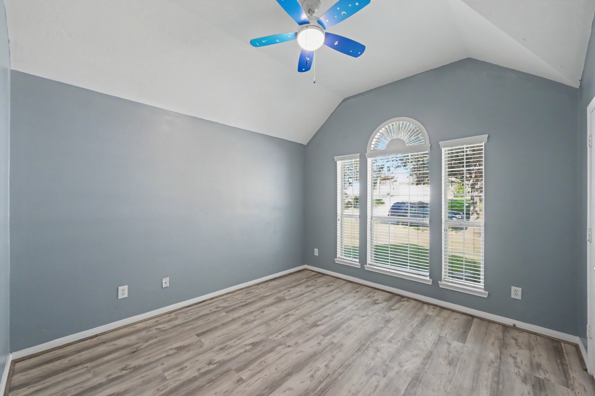 Spacious secondary bedroom featuring vaulted ceilings, wood-look flooring, a decorative arched window and abundant natural light.