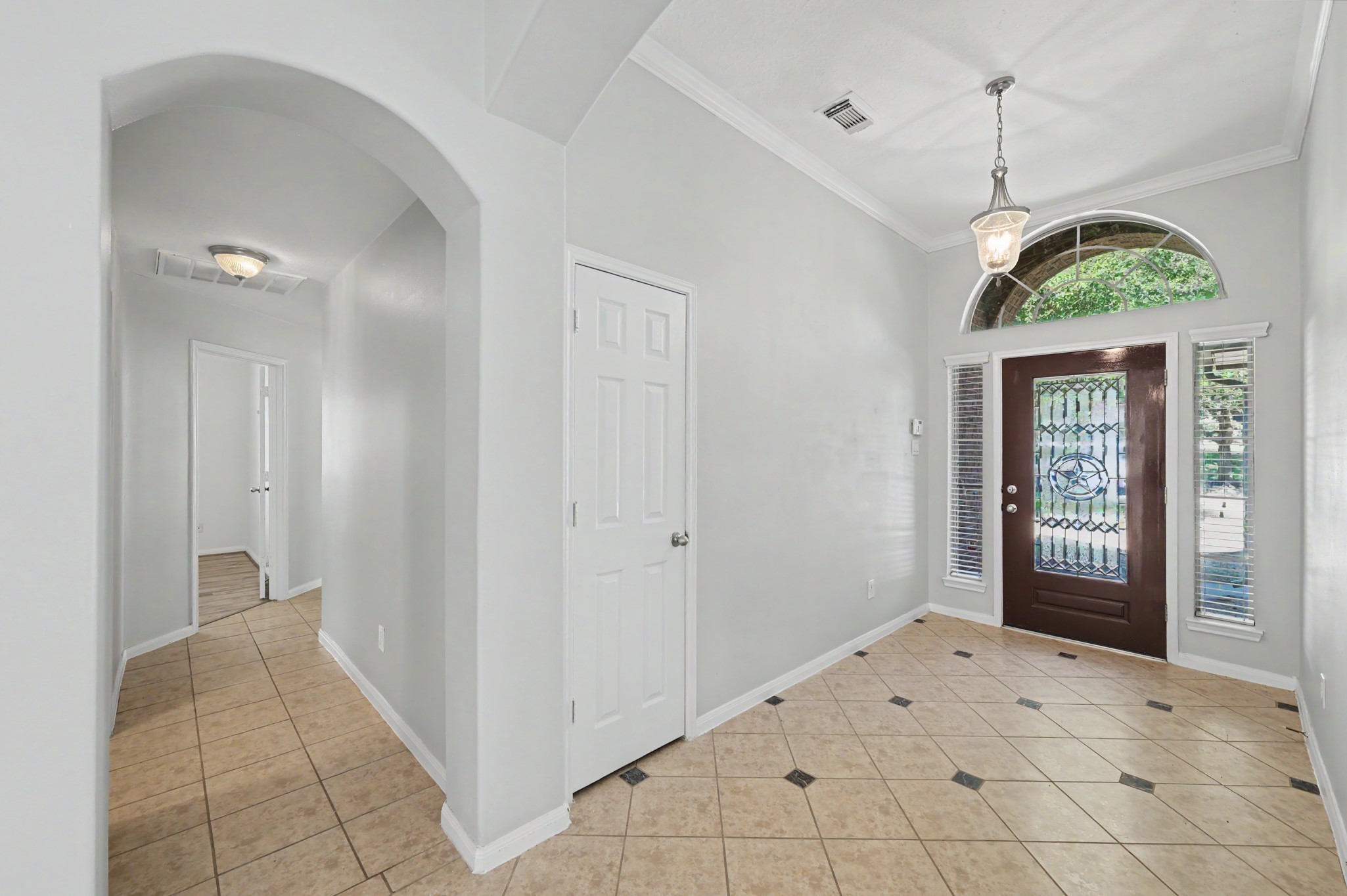 Spacious foyer featuring decorative tile flooring, crown molding, pendant lighting and a beautiful glass front door with arched transom window.