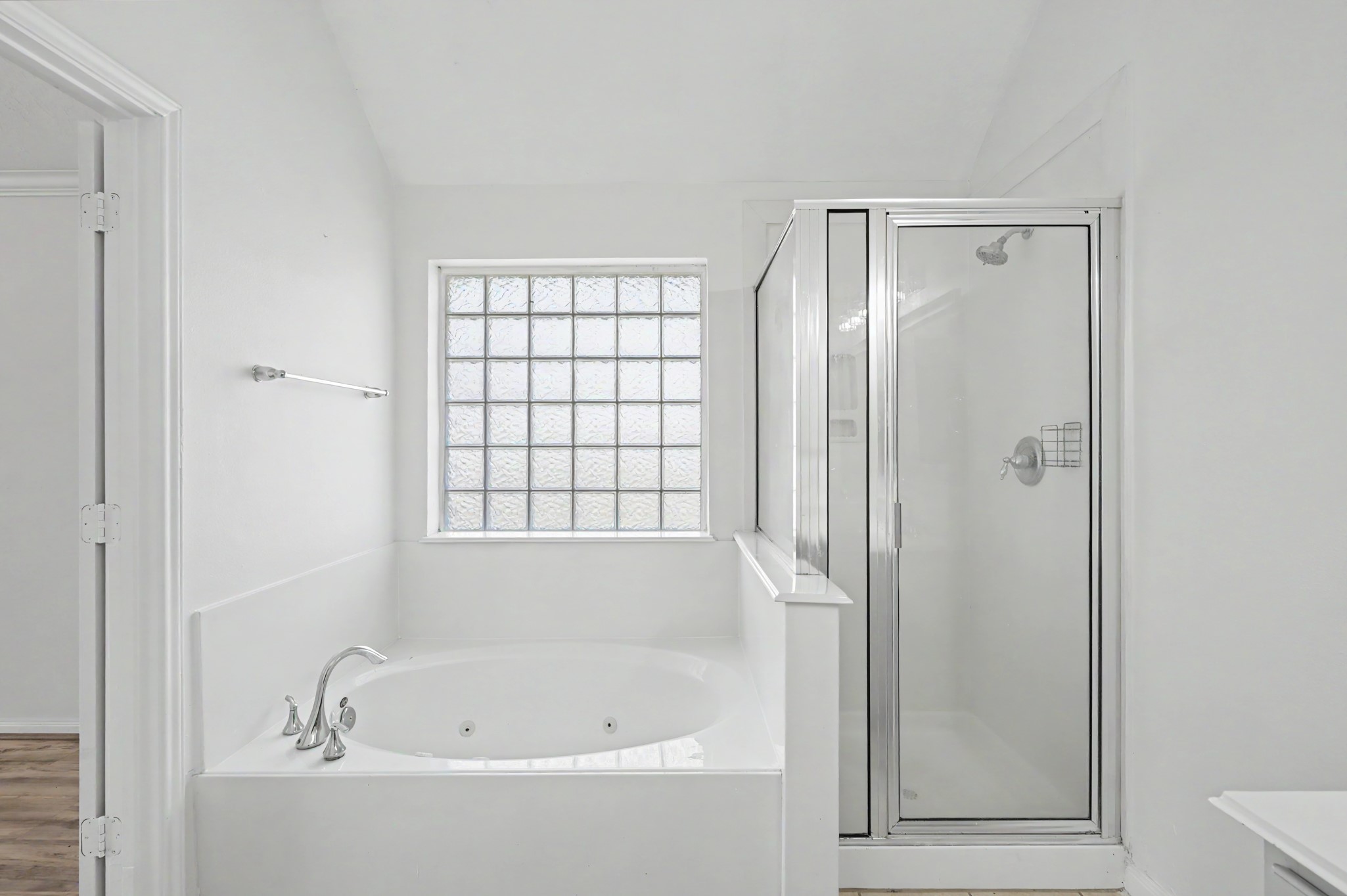 Primary bath featuring a relaxing jetted soaking tub, separate glass-enclosed shower and decorative glass block window.