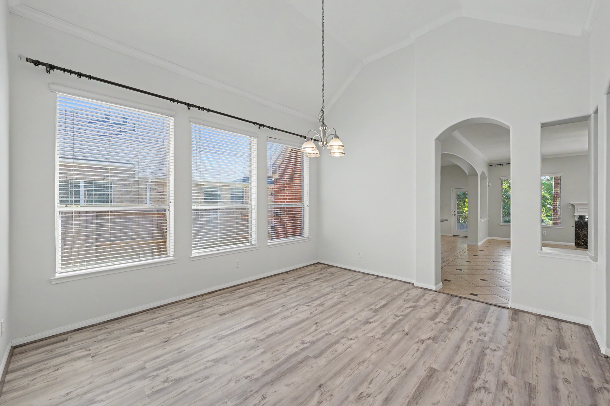 Spacious formal dining room featuring vaulted ceilings, crown molding, wood-look flooring, elegant chandelier and abundant natural light.