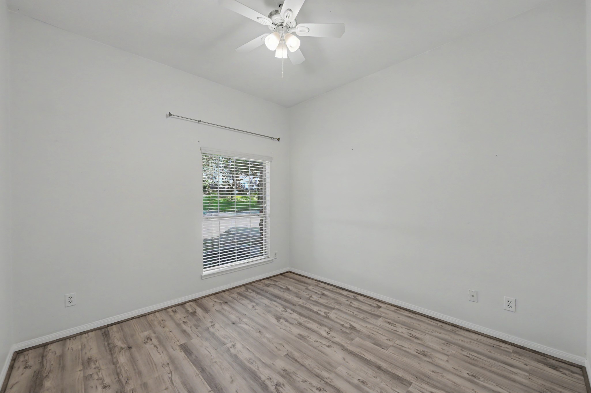 Bright secondary bedroom featuring wood-look flooring, ceiling fan and natural light, perfect for guests or a home office.