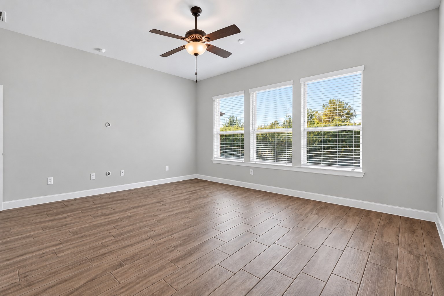Spacious primary bedroom featuring high ceilings, abundant natural light, and beautiful wood-look tile flooring.