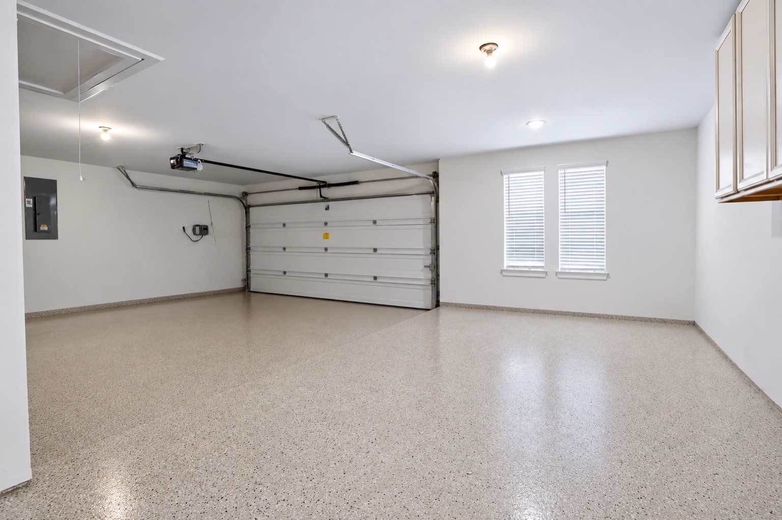 Spacious garage with clean epoxy flooring, built-in cabinetry, and plenty of room for parking and storage.