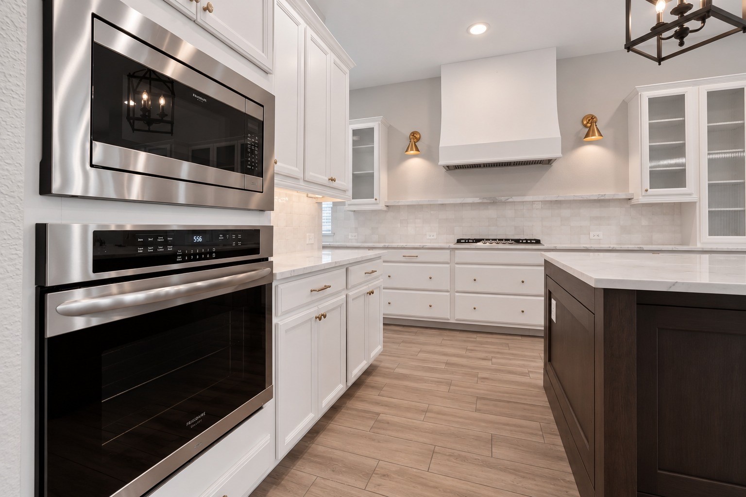 Spacious gourmet kitchen featuring white cabinetry, quartz countertops, a large contrasting island, farmhouse sink, stainless steel appliances, and beautiful gold accents throughout.