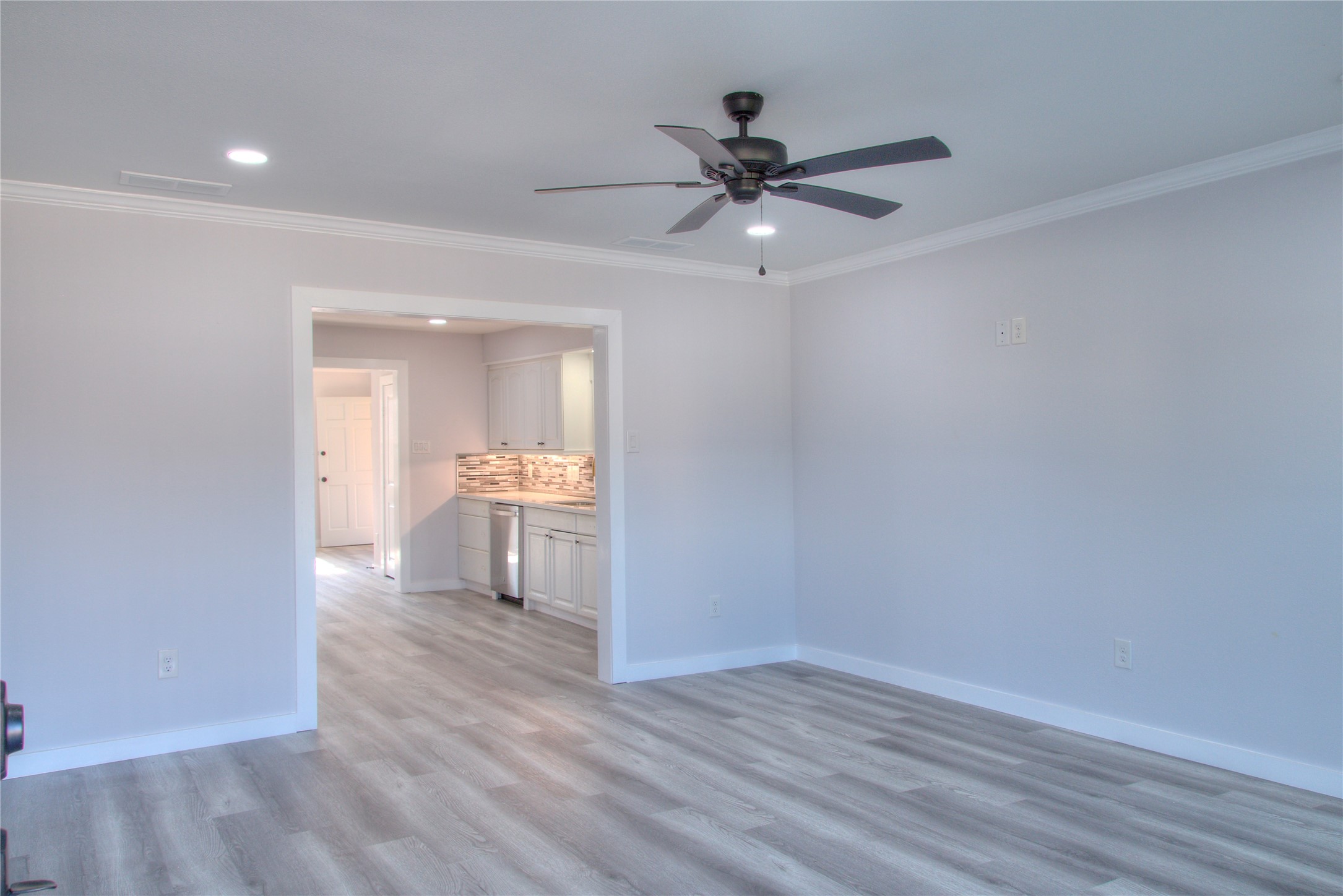 Discover a spacious family room featuring modern updates, including new canister lights, ceiling fan, flooring, baseboards, crown molding, front door, and windows.
