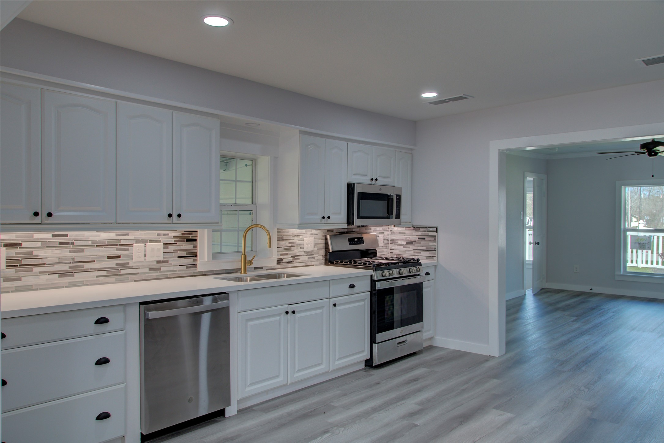 Modern kitchen featuring new stainless steel appliances, quartz countertops, a sleek glass tile backsplash, and under-cabinet lighting.