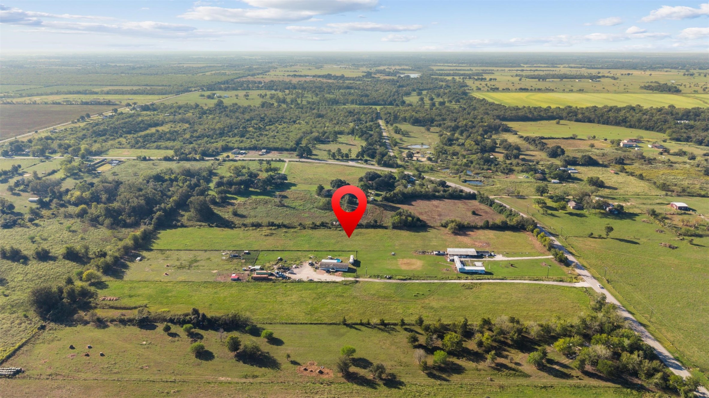South-facing aerial offering a broader perspective of the property's location, with FM 1887 winding through the surrounding countryside and a patchwork of pastures, wooded tracts, and rural homesteads.