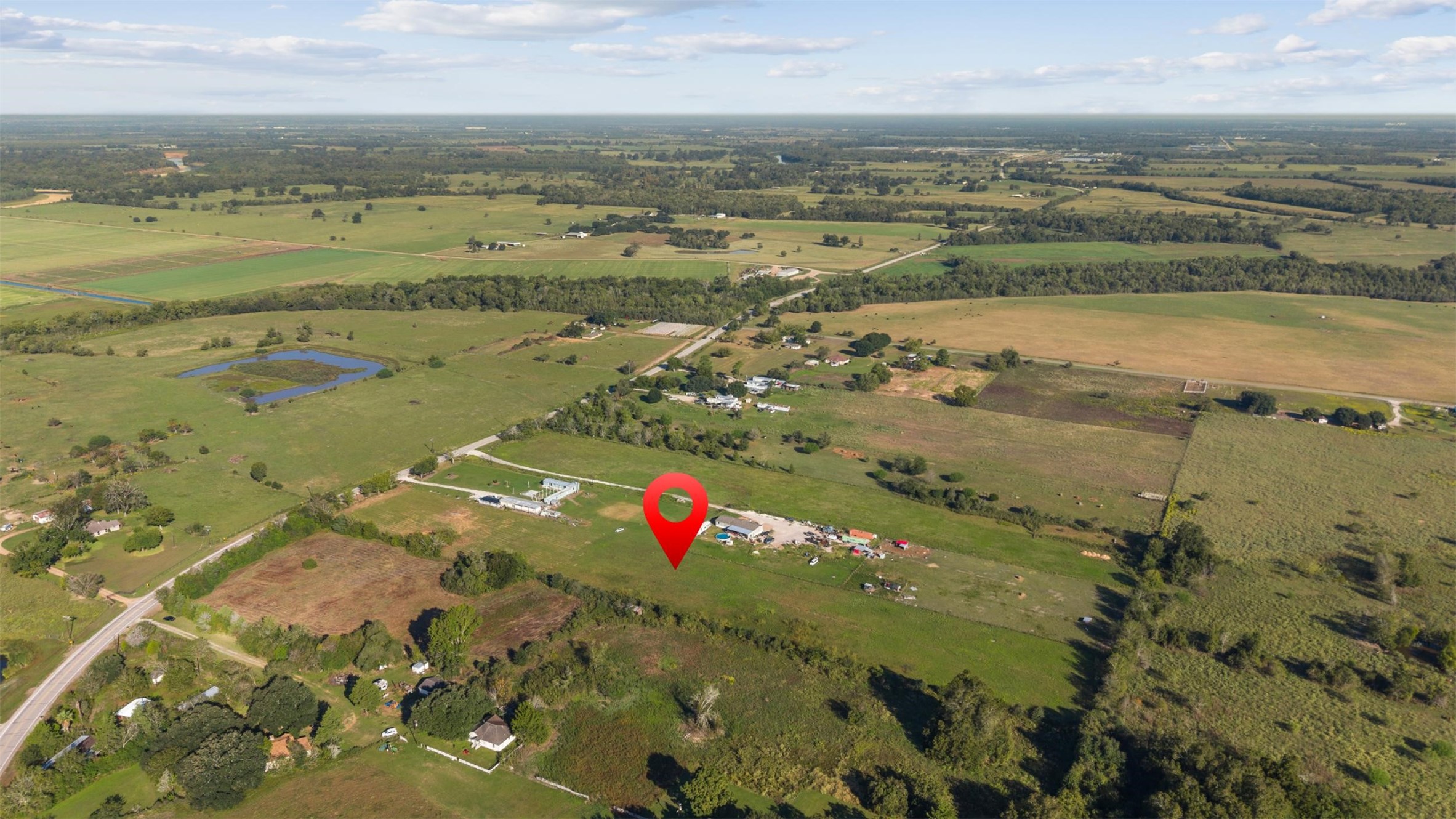 Northwest-facing aerial capturing the property's setting among expansive agricultural fields, neighboring homesteads, and a mix of wooded landscapes and open countryside.