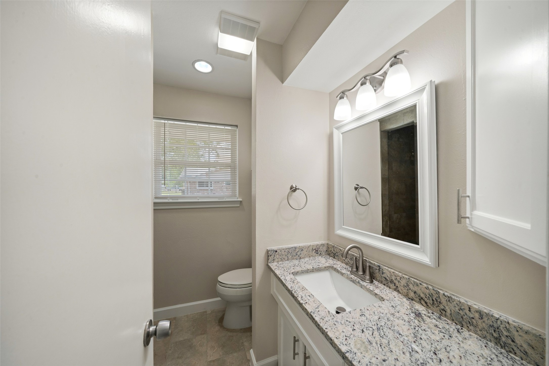 This bright and refreshed primary bathroom features a clean, neutral design with a spacious vanity and plenty of natural light. The vanity has been updated with newly installed Dallas White granite countertops, complemented by brushed nickel faucets and fixtures for a modern finish. A large white-framed mirror and coordinated lighting complete the polished, updated look.