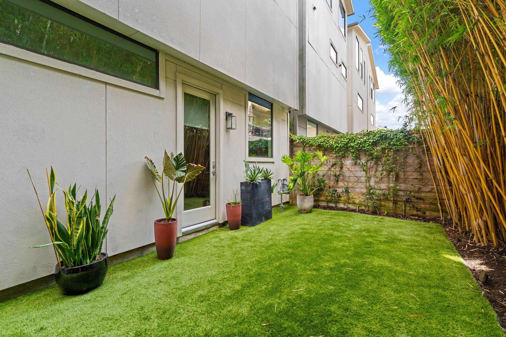 Generously sized, low-maintenance backyard features artificial turf, professional landscaping, privacy-enhancing bamboo, and direct access from a first-floor bedroom.