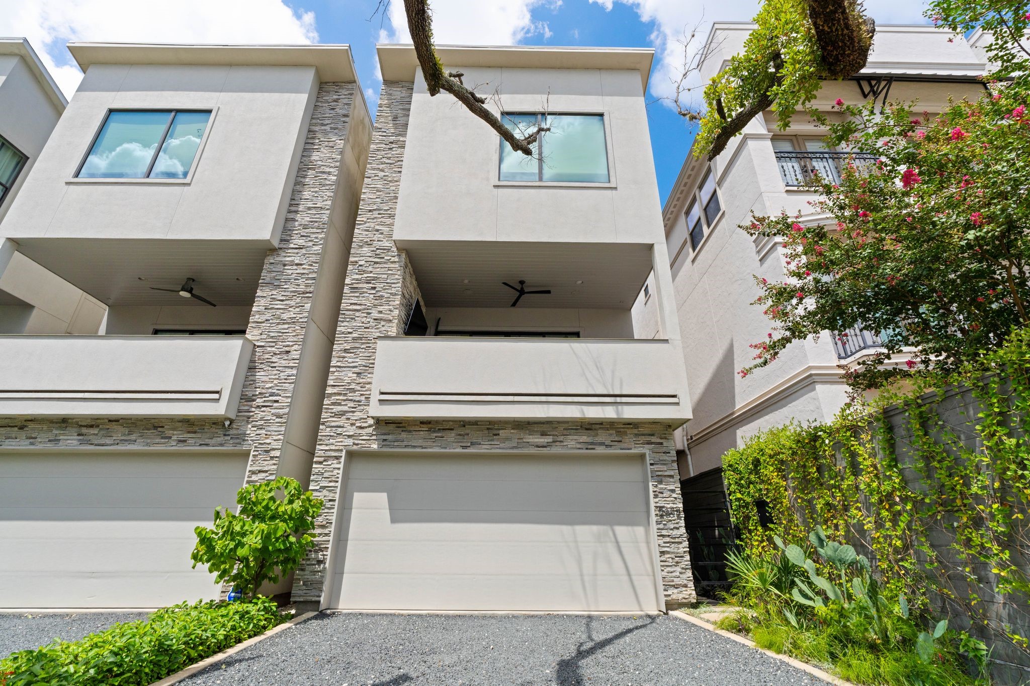 Contemporary front elevation with professional landscaping, mature oak tree, private gravel driveway, and oversized two-car garage with additional storage.