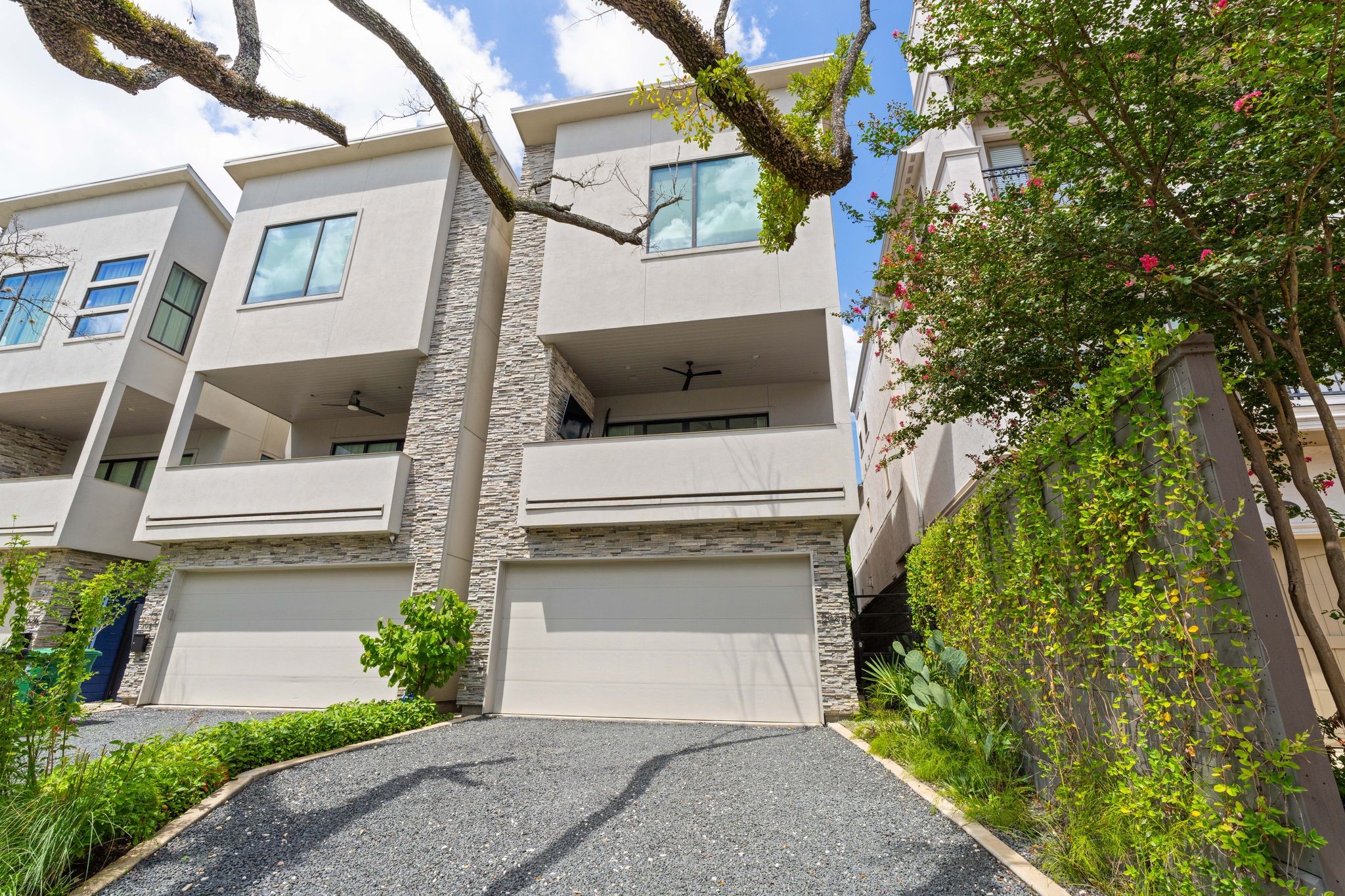Contemporary Upper Kirby residence framed by mature oak trees, professional landscaping and climbing greenery, with a private gravel driveway and second-floor covered terrace.