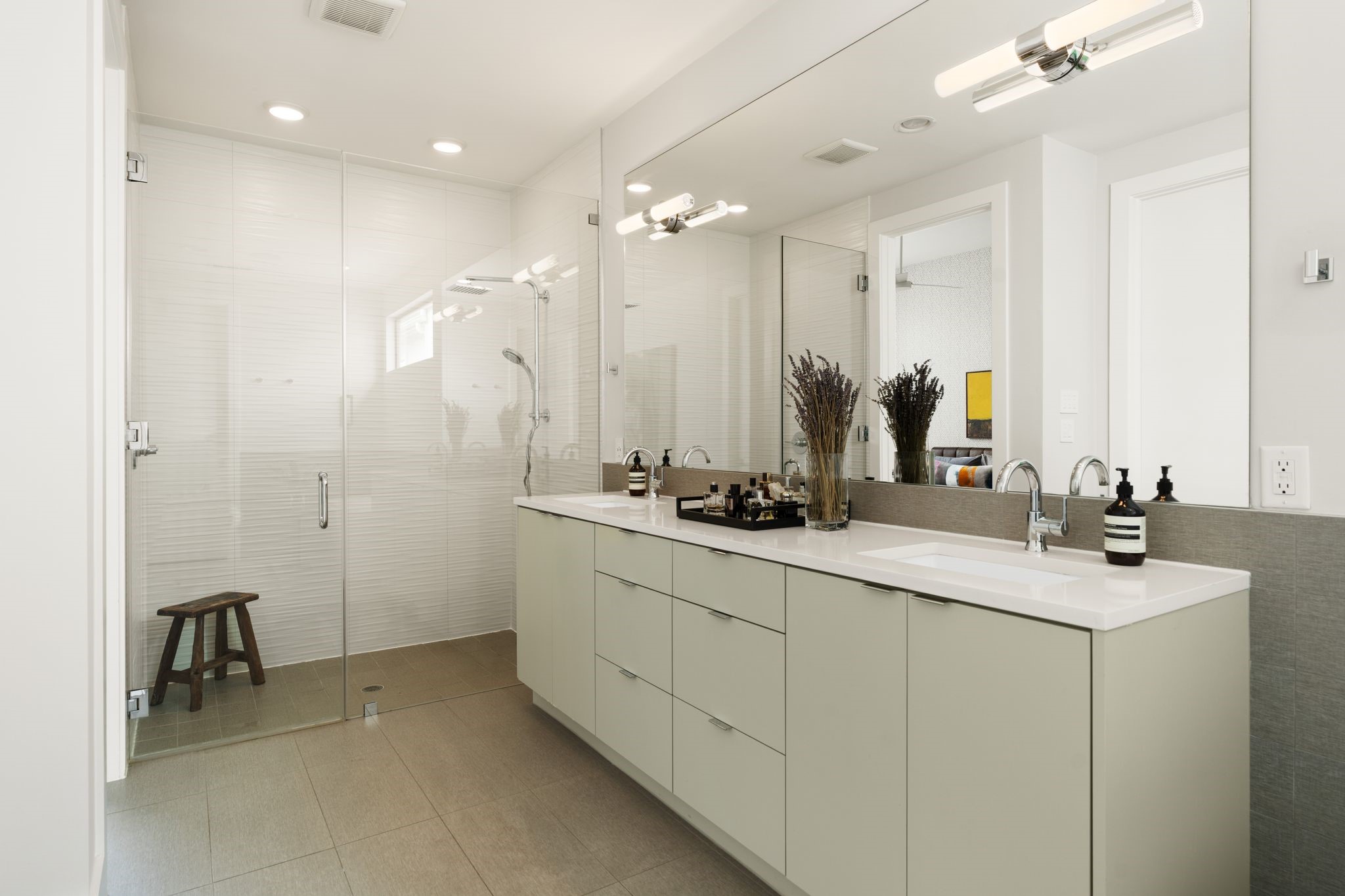 Luxurious primary bath with high ceilings, glass-enclosed shower, expansive double-sink vanity, and abundant custom cabinetry and drawer storage.
