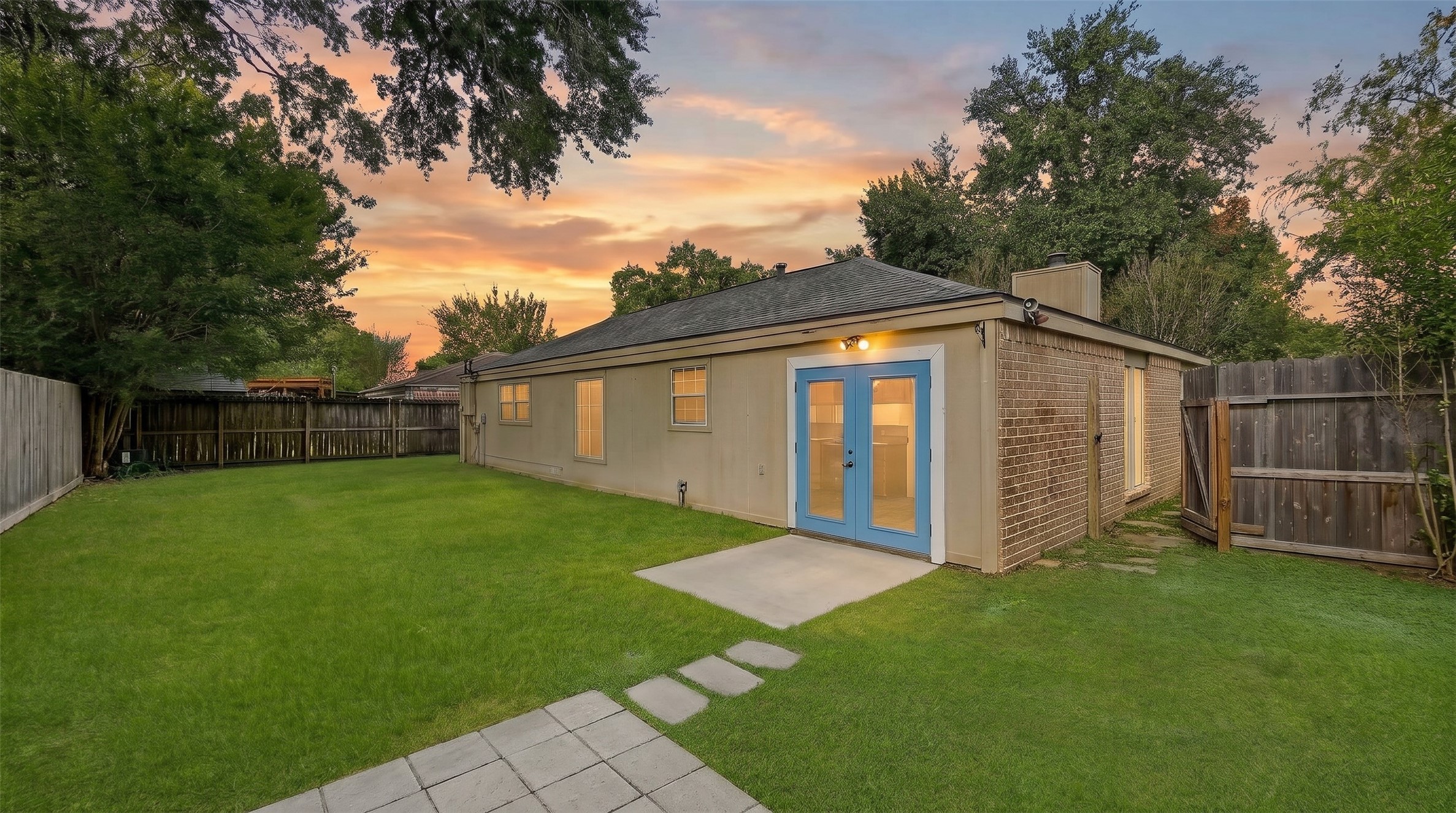 Embrace relaxed outdoor living in this serene, fully fenced backyard haven, surrounded by leafy canopy trees and sprawling green lawn. A charming stone path connects paved open-air patios, offering ideal spots for weekend grilling or twilight gatherings.
