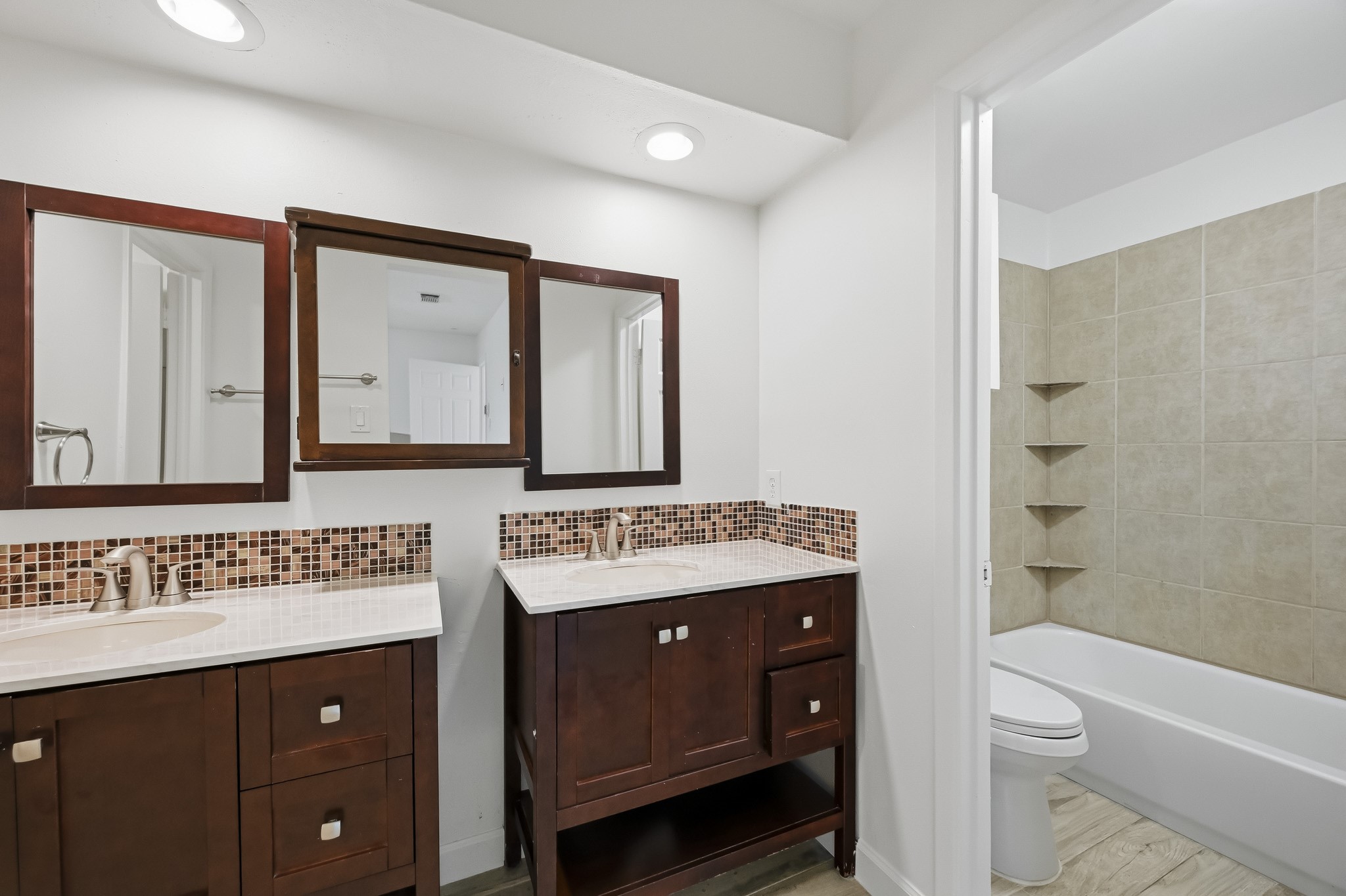 Brightened by overhead recessed lighting, the open layout leads into an adjoining wet area featuring a tub-shower combination with floor-to-ceiling tiling and built-in corner shelves.