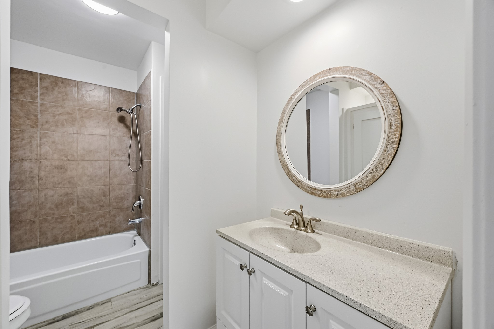 This secondary bathroom combines everyday comfort with a clean, functional layout. The grooming area features an expansive vanity counter with an integrated basin and under-counter storage, highlighted by a decorative circular mirror and overhead lighting