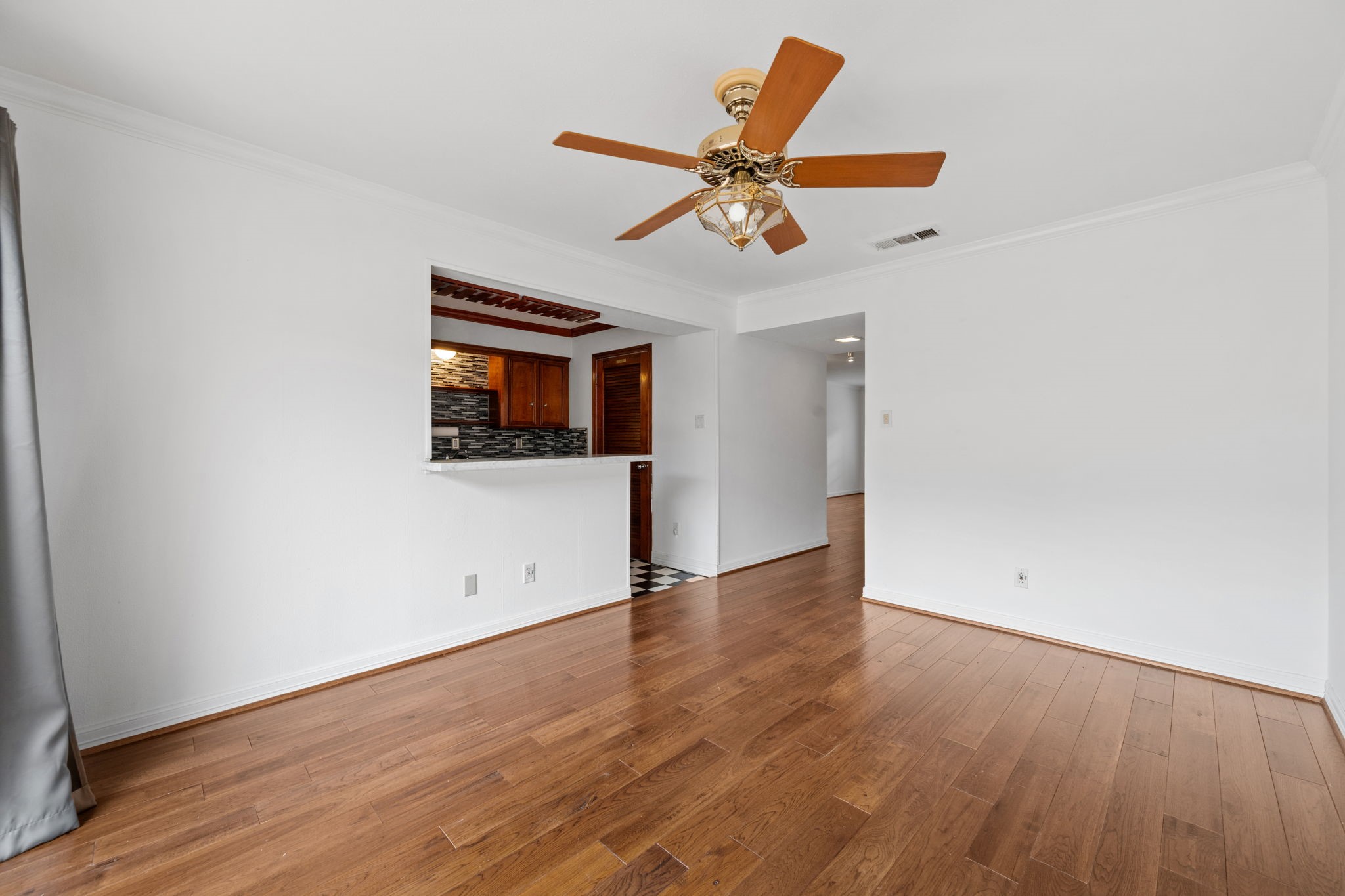 Bright and inviting living space with elegant hardwood floors, a stylish ceiling fan, and a pass-through window to the kitchen, enhancing openness and connectivity.