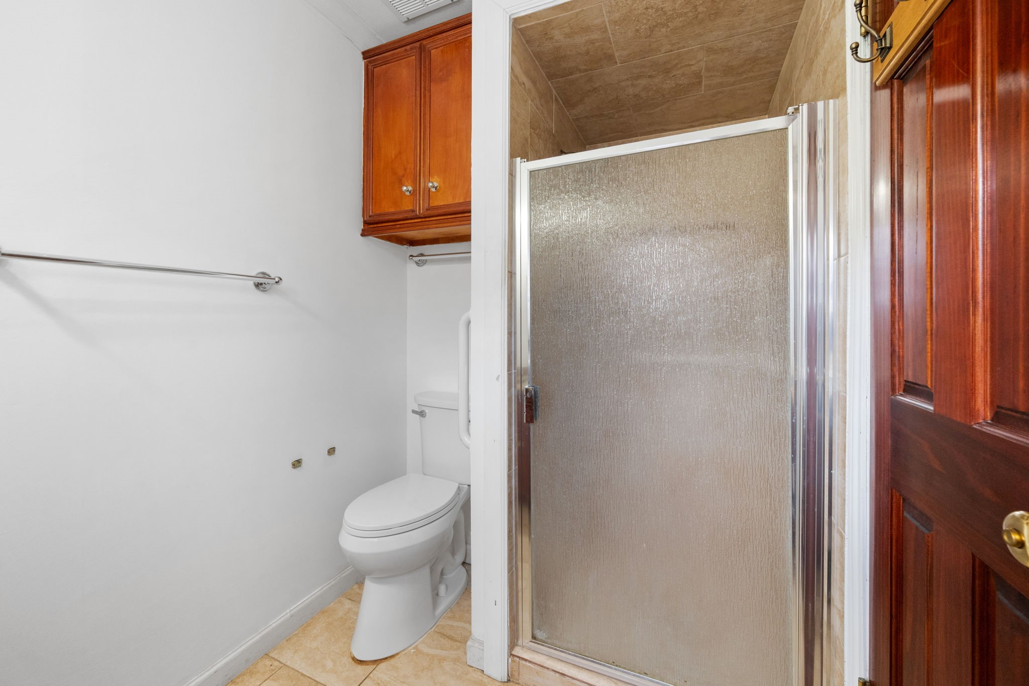Cozy bathroom featuring a walk-in shower with frosted glass door, elegant wooden cabinetry, and a classic white toilet.
